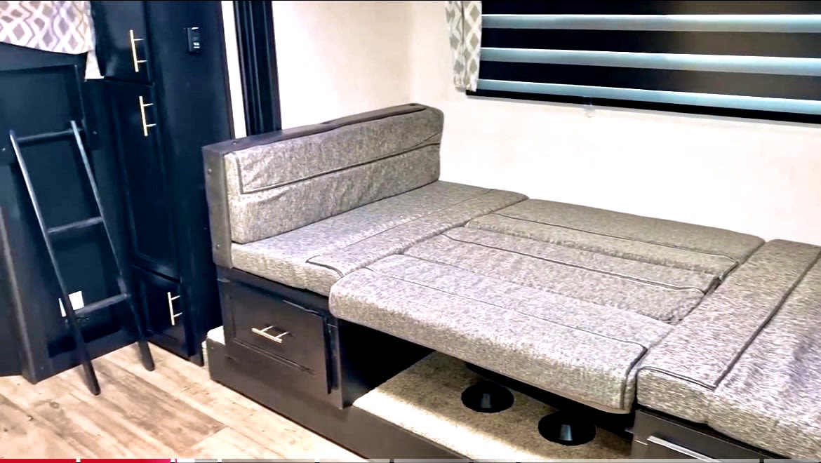 RV rental interior view: Gray modular sofa converts to a bed. Dark cabinetry with bunk ladder on left.. Forest River Cherokee Grey Wolf 2022