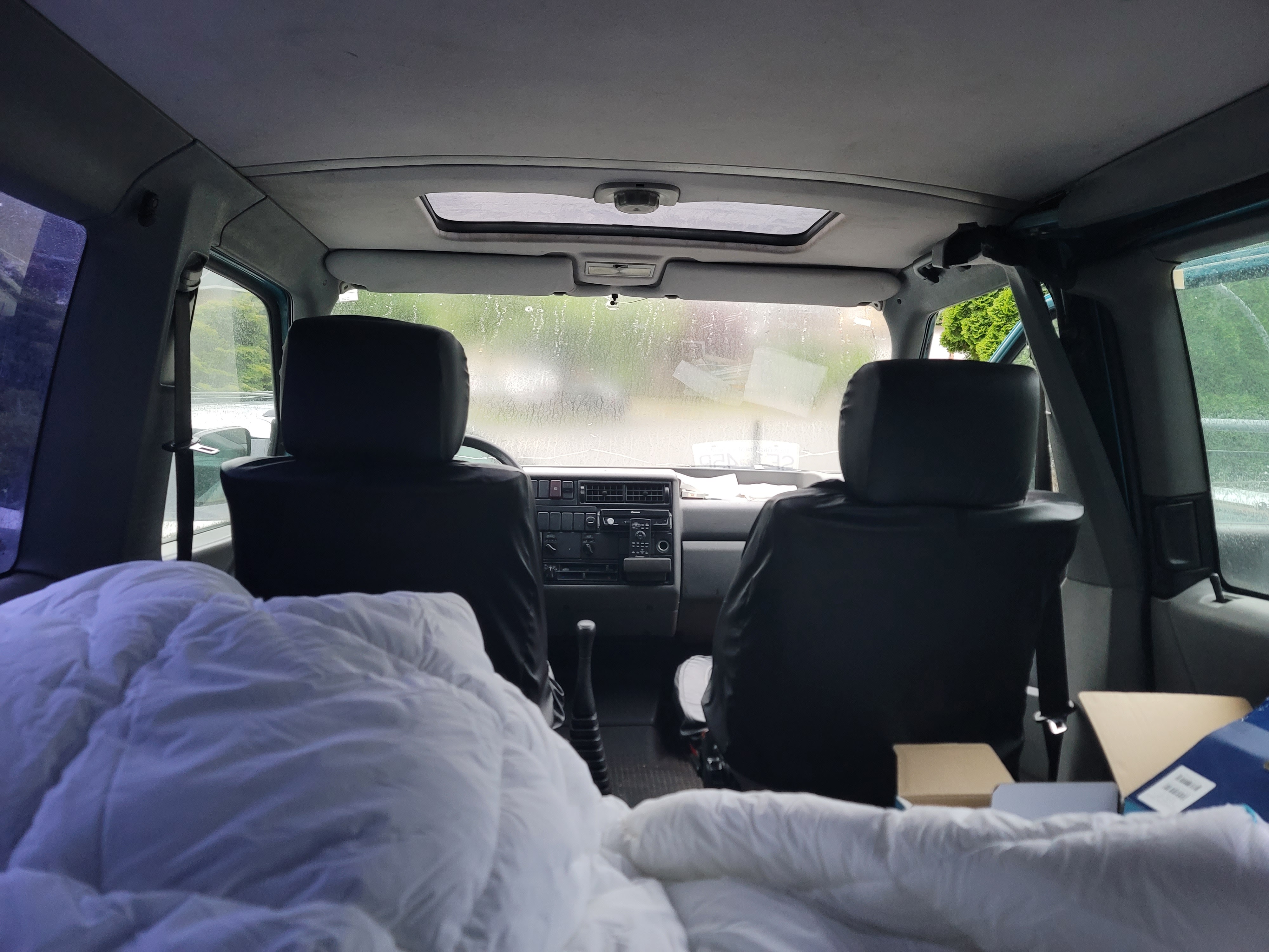 Cozy RV rental interior with a white duvet, dashboard view through a misty windshield and sunroof.. Volkswagen Eurovan 1992