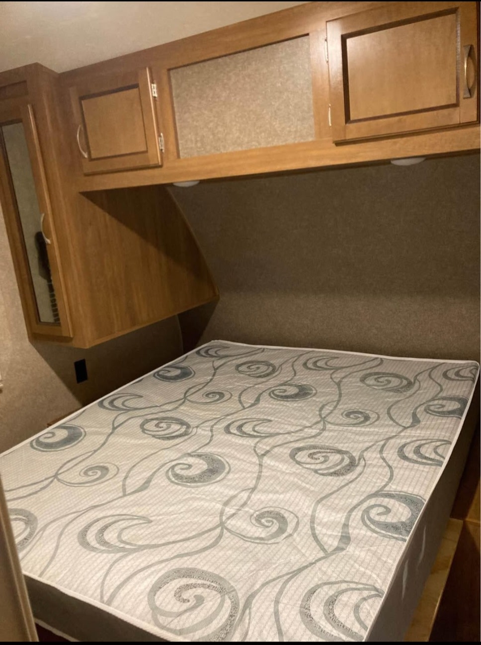 RV rental bedroom featuring a patterned mattress, wooden overhead cabinets, and integrated lighting above the bed.. Forest River Coachmen Catalina Legacy 2019