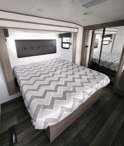This comfortable RV rental bedroom features a large bed with a stylish chevron comforter, a dark headboard, and mirrored closet.. Heartland RVs Elkridge 2022