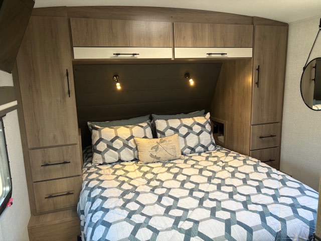 Inside a comfortable **RV rental** bedroom, featuring geometric patterned bedding, built-in cabinets, and soft ambient lights.. Grand Design Imagine 2024