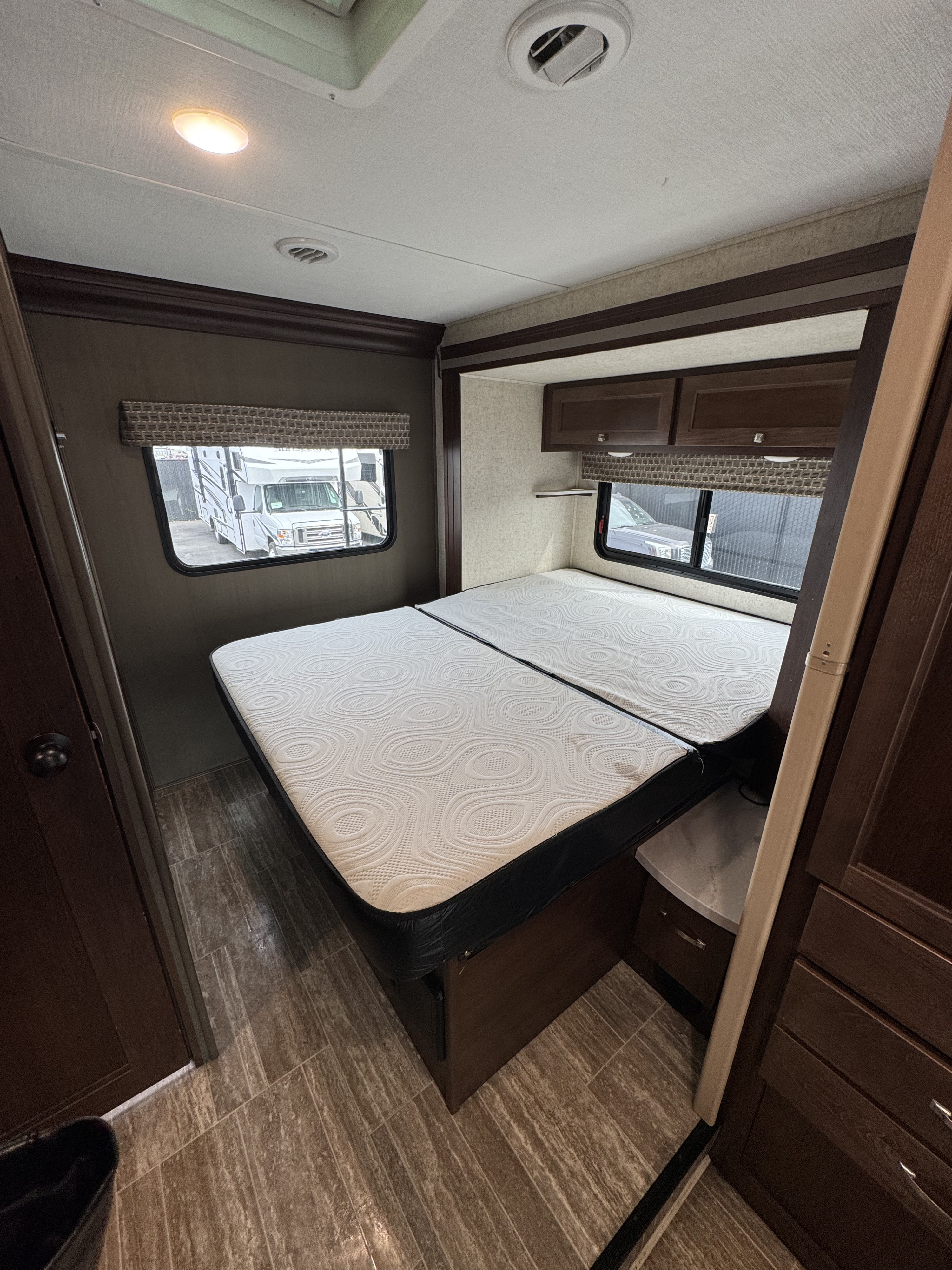 RV rental bedroom: two white patterned mattresses, dark wood cabinetry, window views, and light-colored ceiling.. Forest River Sunseeker LE 2020