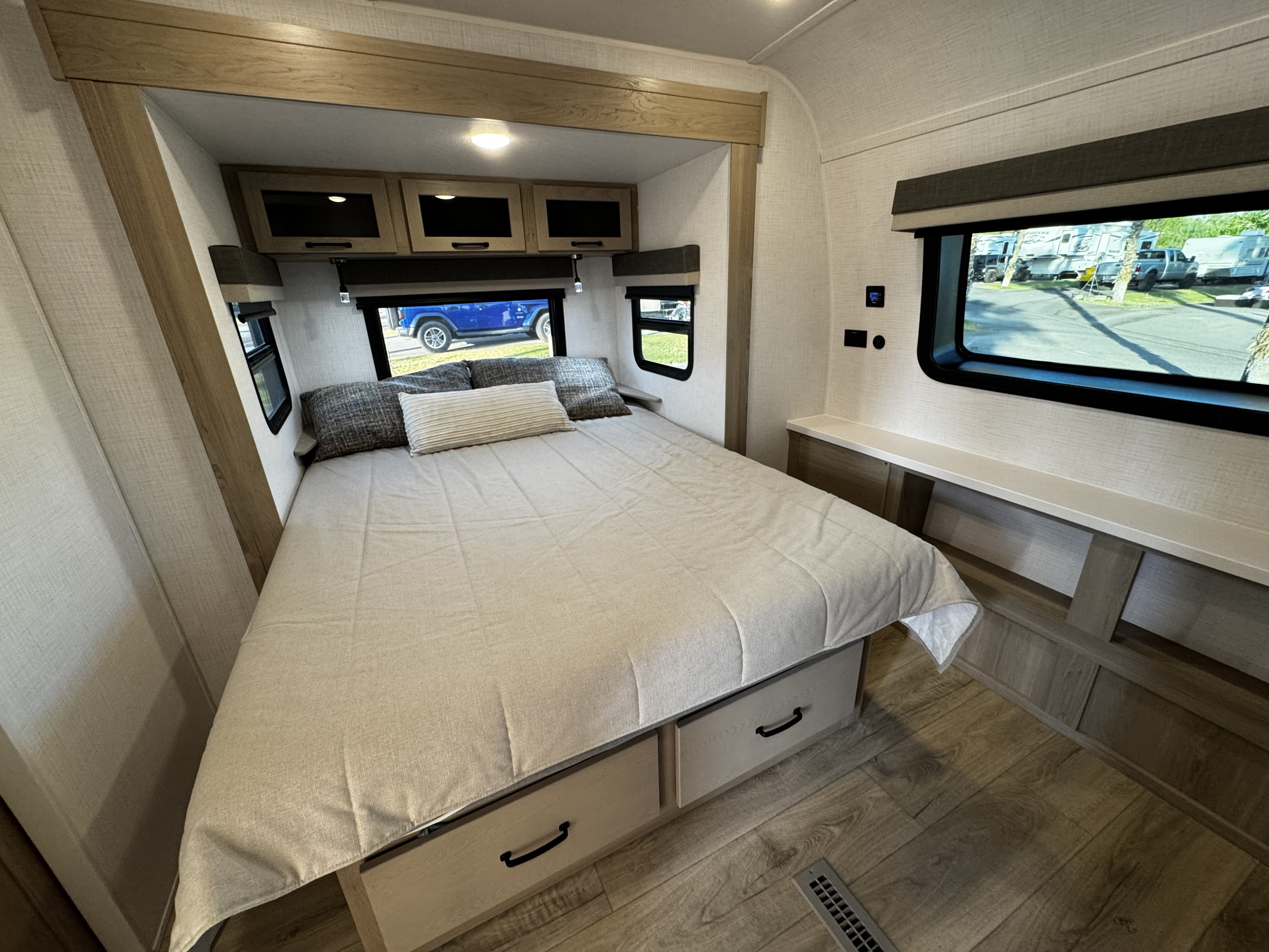 Cozy RV rental bedroom featuring a large bed with under-bed storage, overhead cabinets, and windows with scenic views.. Forest River Rockwood Ultra Lite 2024