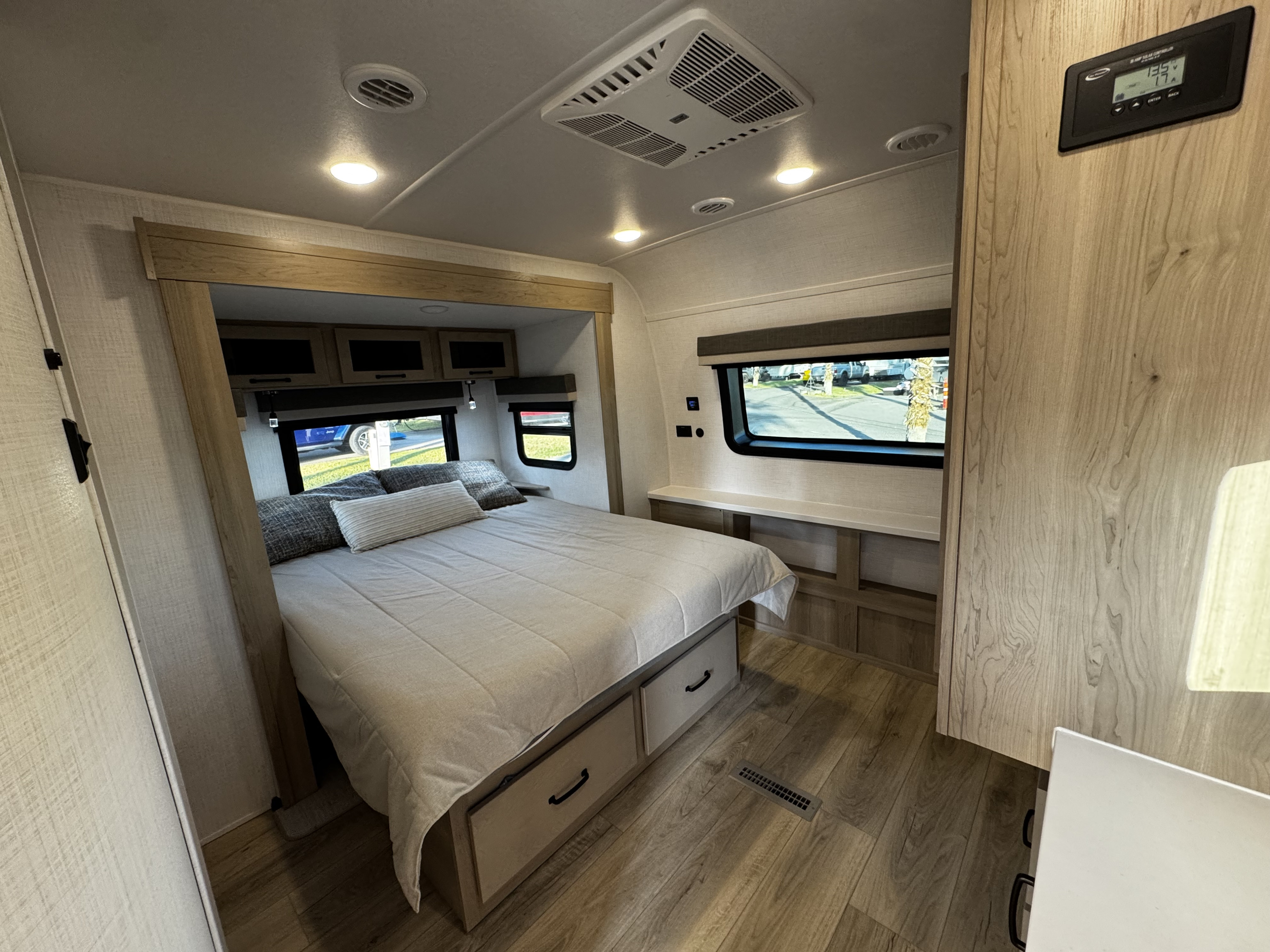 Modern RV rental bedroom with a queen bed, under-bed storage, and bright windows, plus a solar panel controller on the wall.. Forest River Rockwood Ultra Lite 2024