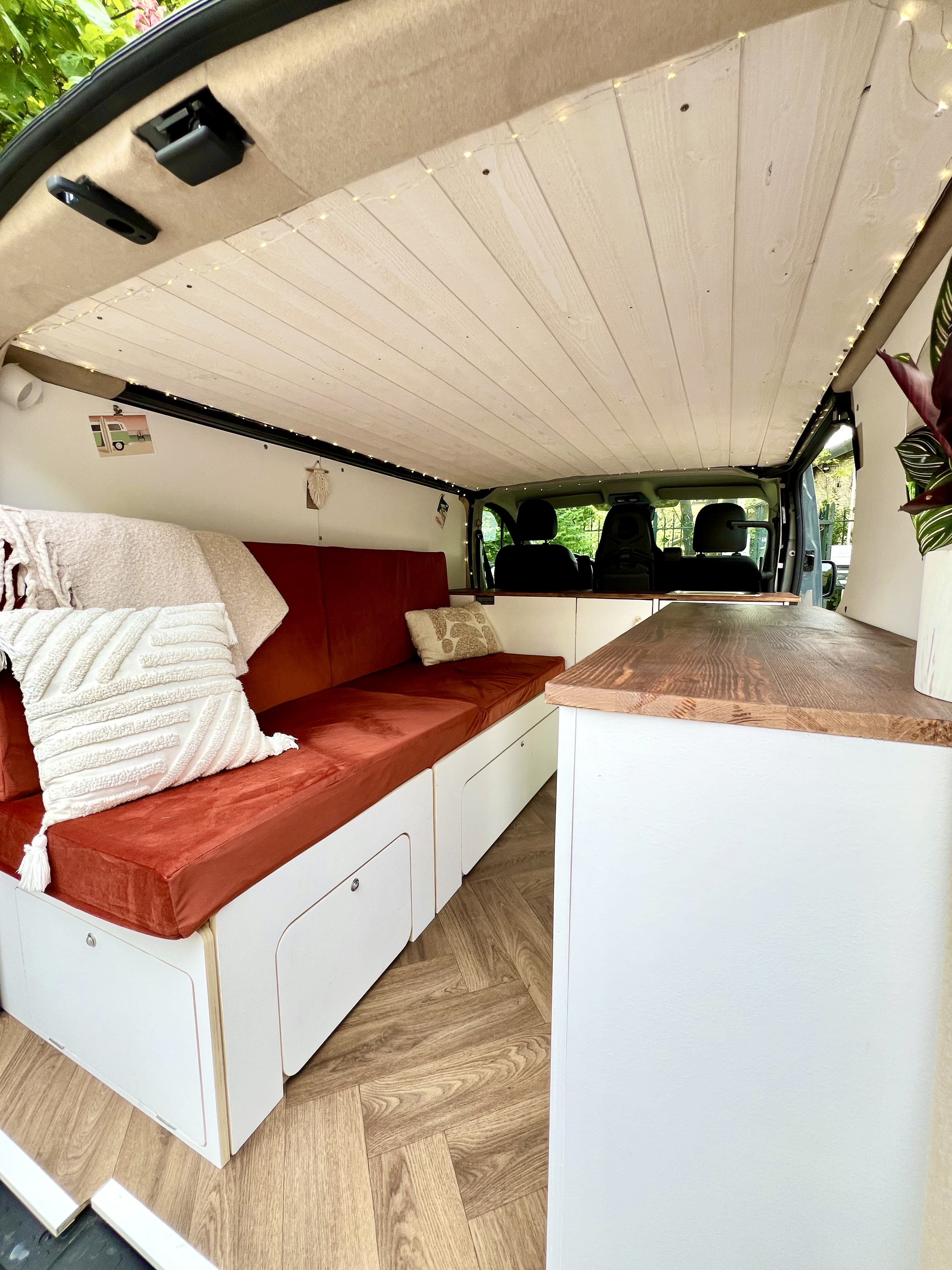 Cozy RV rental interior showcasing custom-built features: burnt orange cushions, wooden ceiling with lights, and herringbone floor.. Renault Trafic 2023