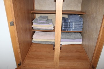 An open RV rental cabinet reveals neatly stacked, folded fresh linens including towels and blankets on its shelves, ready for use.. Jayco Eagle Super Lite 2010