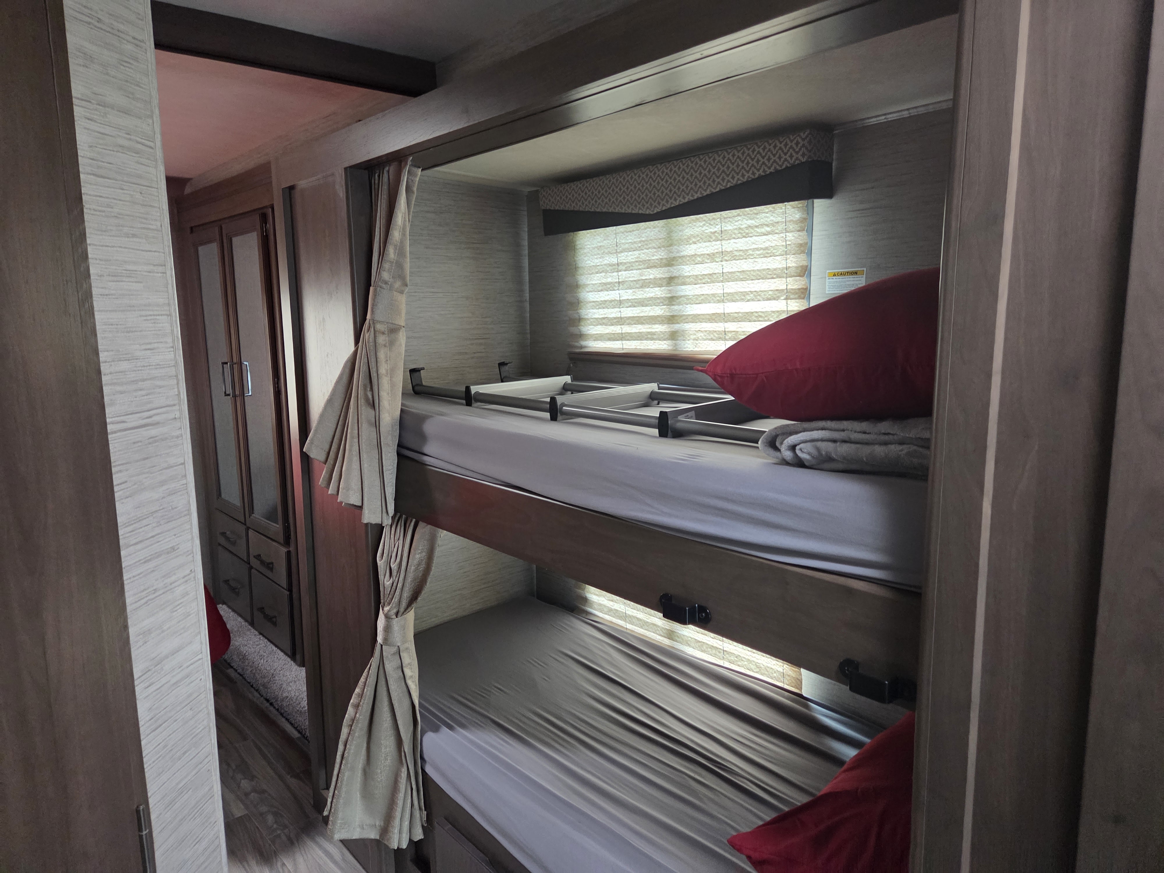 Compact bunk beds inside an RV rental, perfect for family travel. Features a ladder, window, and small wardrobe.. Thor Four Winds 2021