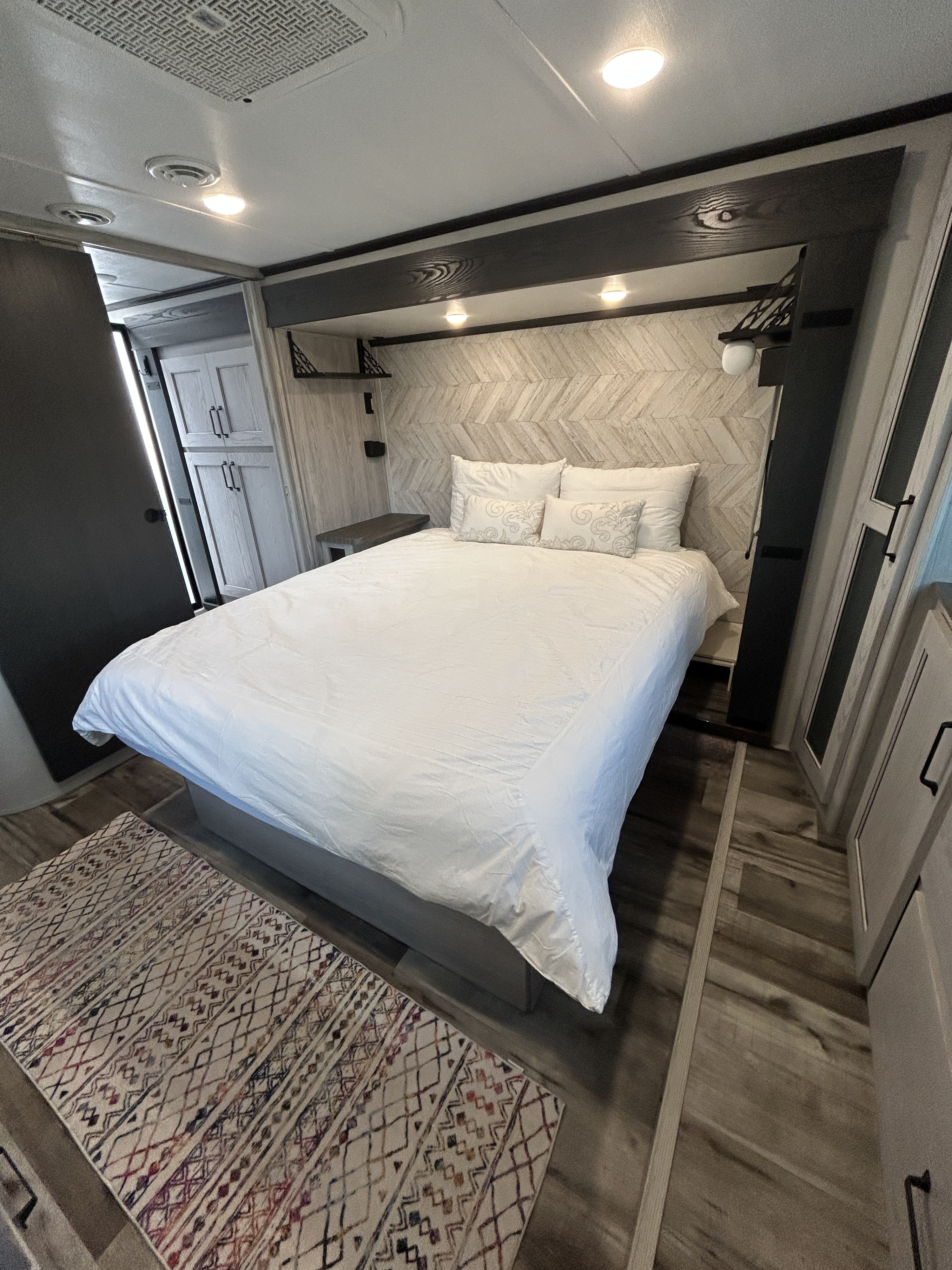 Modern RV rental bedroom with white bedding, chevron headboard, and storage. Perfect for a comfortable stay.. Keystone RV Montana High Country 2023