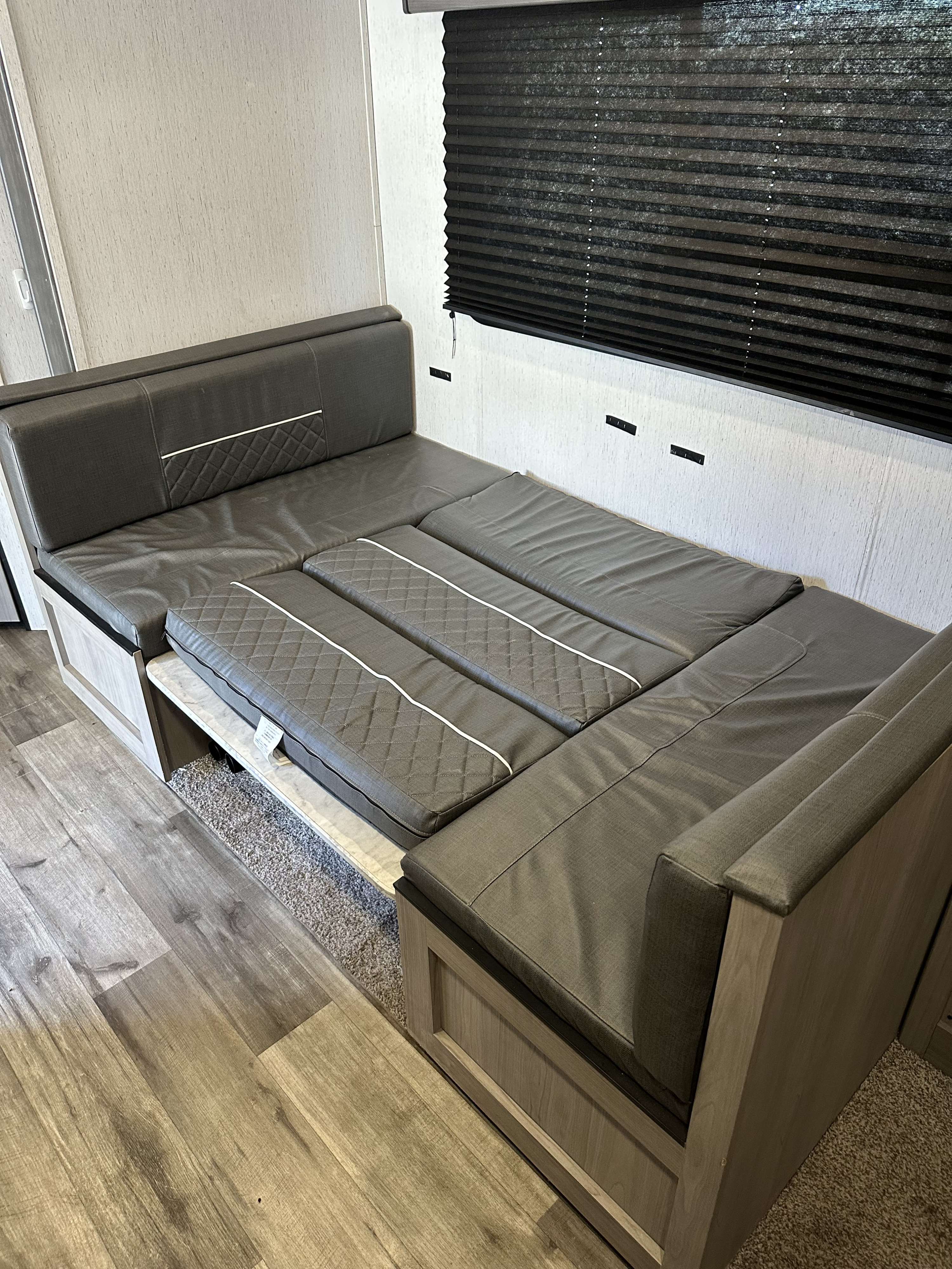 Inside an RV rental: A grey upholstered dinette, featuring quilted cushions, converts into a spacious bed.. Dutchmen Coleman Lantern 2022