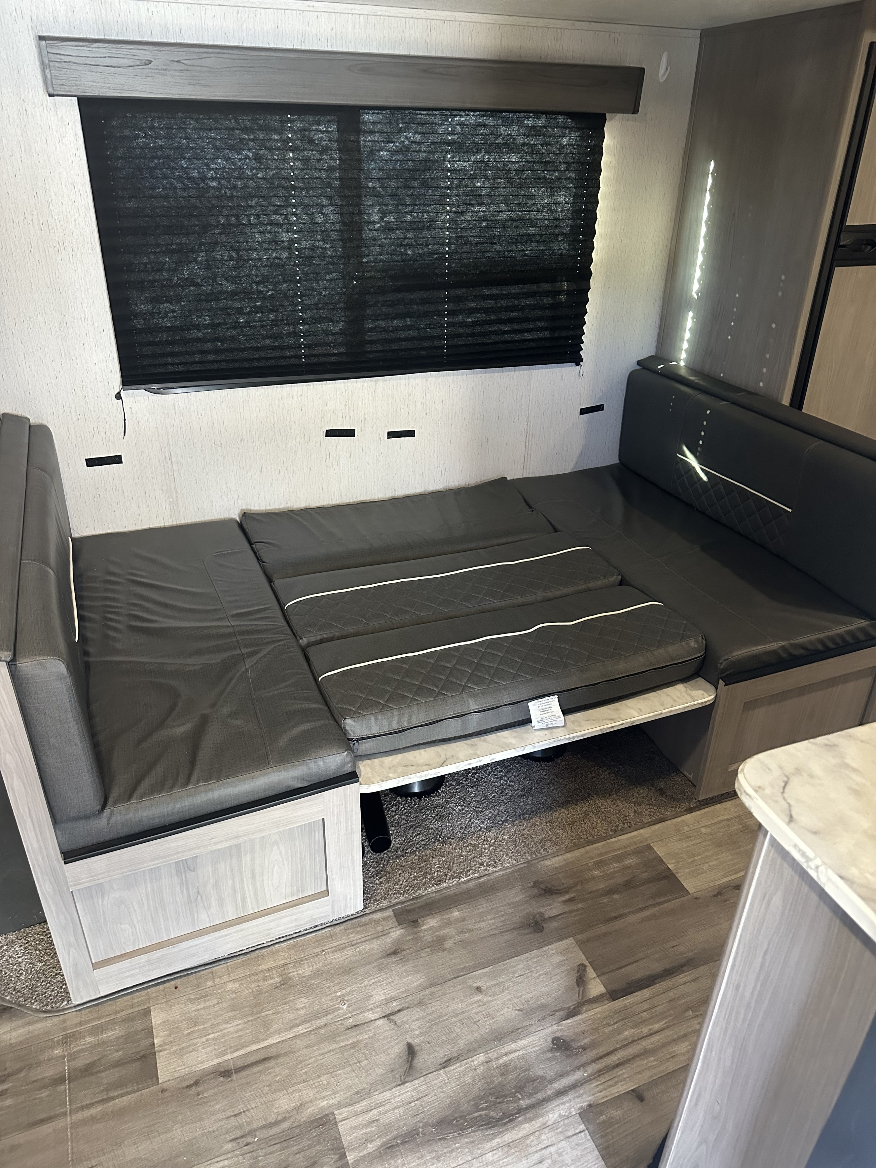 RV rental interior featuring a versatile dinette/lounge area with dark cushions, convertible to a bed, and a large window.. Dutchmen Coleman Lantern 2022