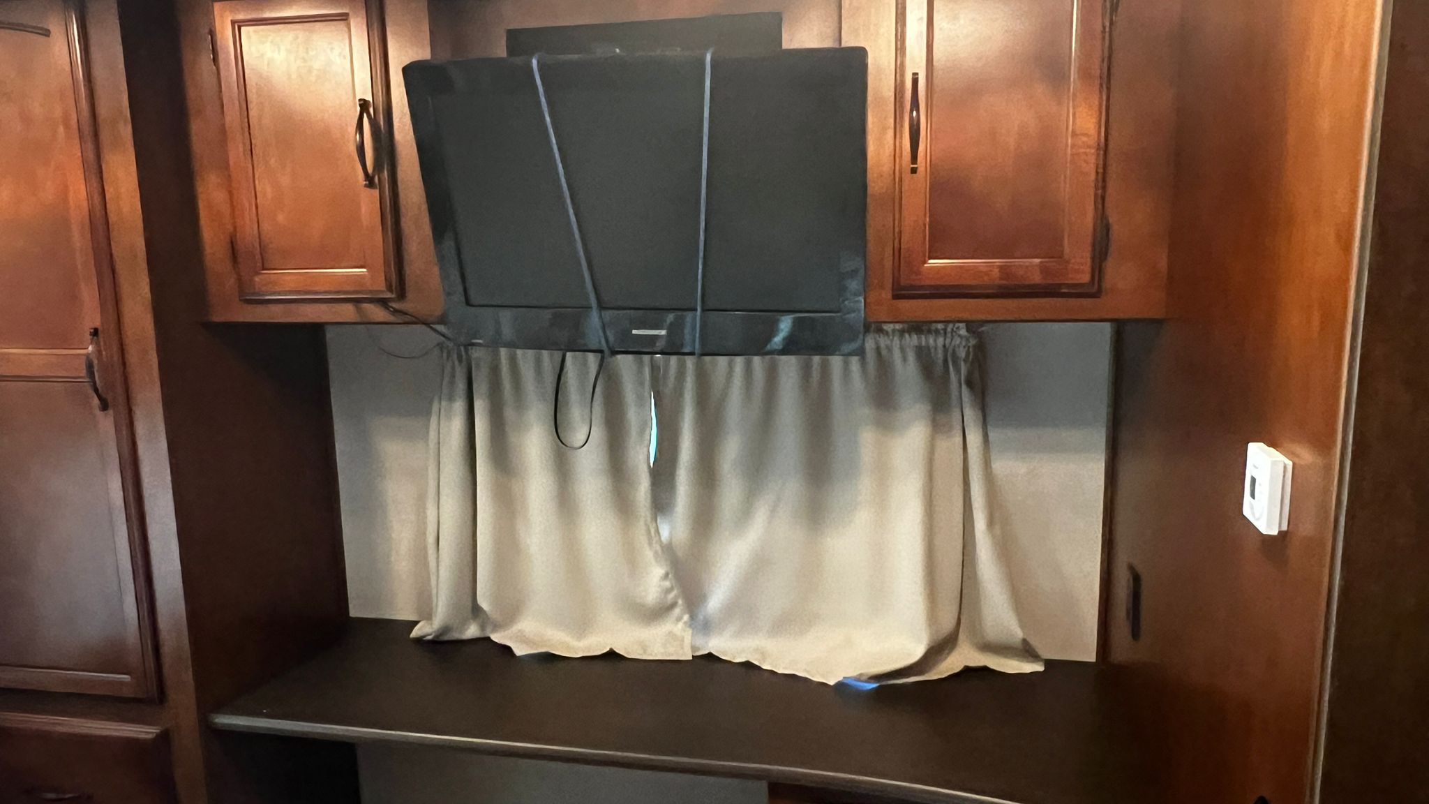 Inside an RV rental: Secured TV, wooden cabinets, desk space, and curtains, ready for your next adventure in this camper.. Forest River Coachmen Mirada 2012