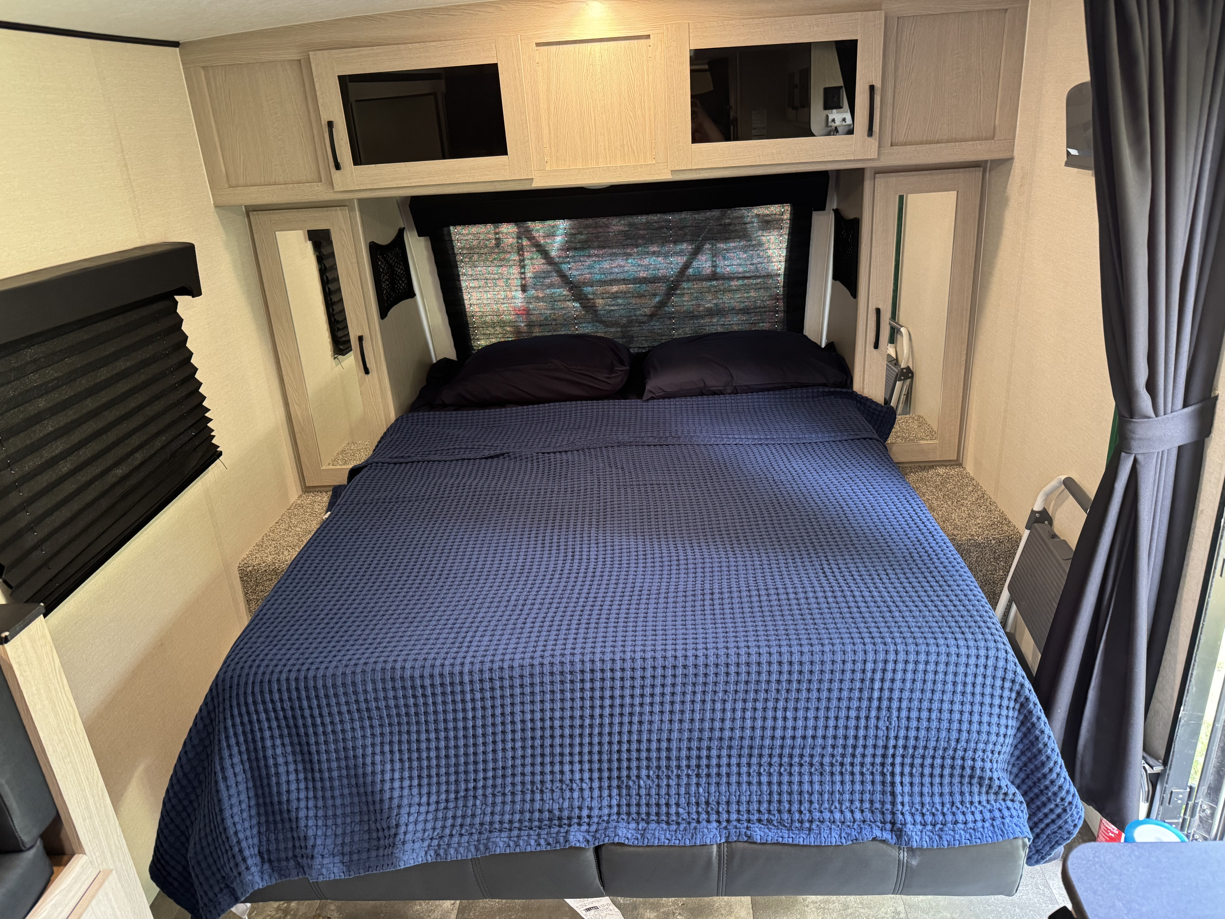 Cozy RV rental bedroom featuring a bed with a blue waffle-knit blanket, black pillows, and light wood cabinetry.. Coachmen Apex Nano 2022