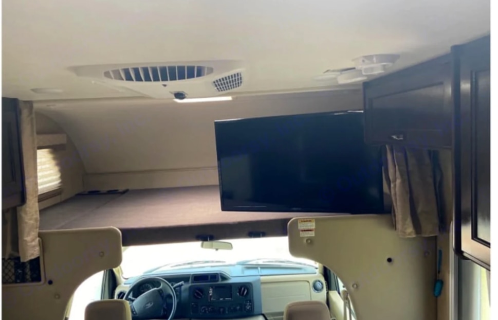 Inside an RV rental: view of the cab-over bunk, large screen TV, and driver's cockpit. Ideal for comfortable travel.. Coachmen Freedom Elite 2019