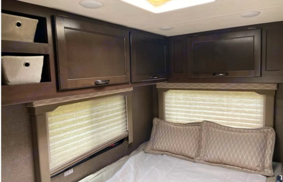 Cozy RV rental interior: Bedroom with dark cabinets, entertainment unit, windows, and bed. Practical storage for travel.. Coachmen Freedom Elite 2019