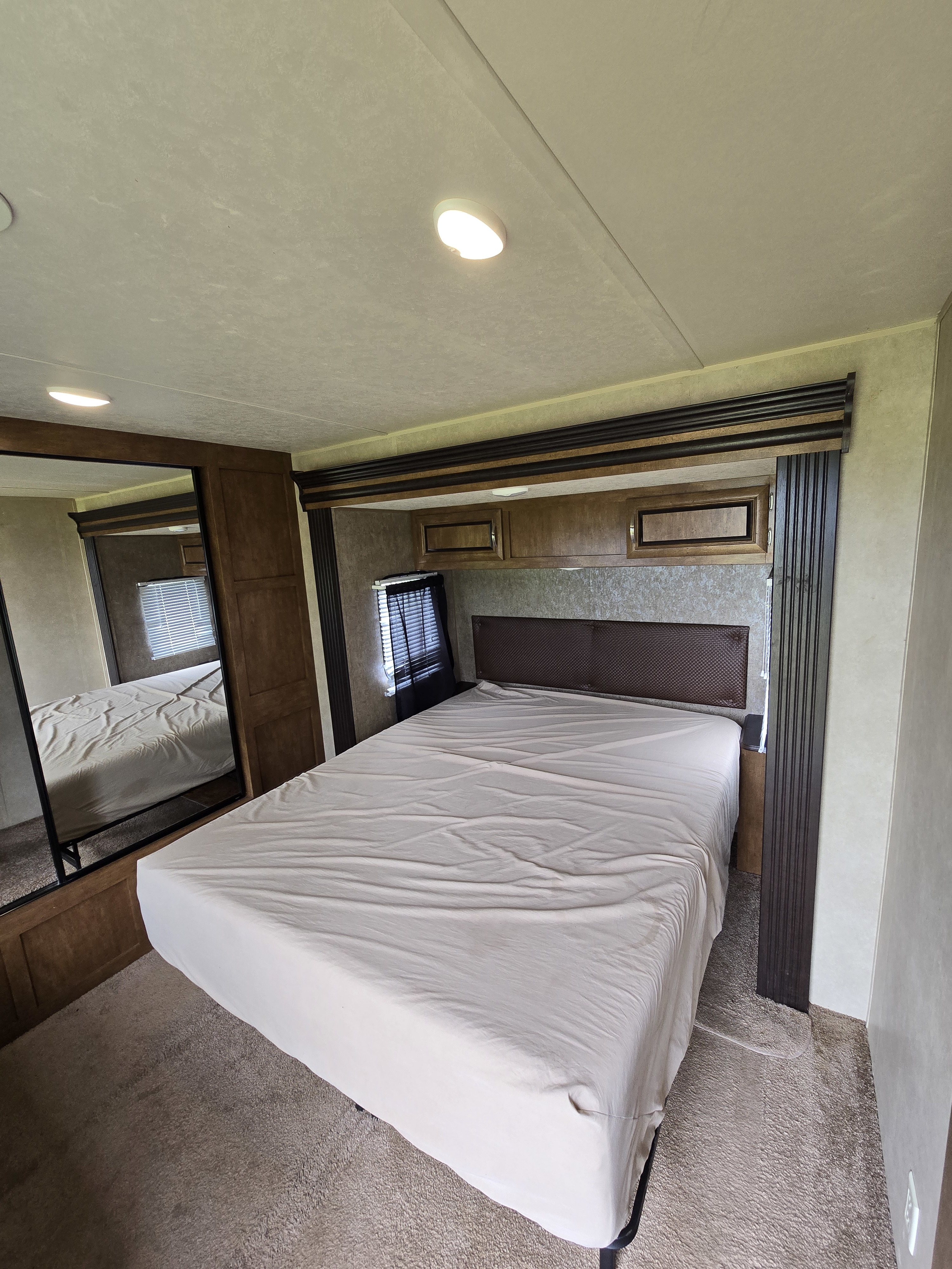 Comfortable RV rental bedroom with a queen bed, overhead cabinets, and mirror. Ideal for your next adventure.. Forest River Wildwood 2016