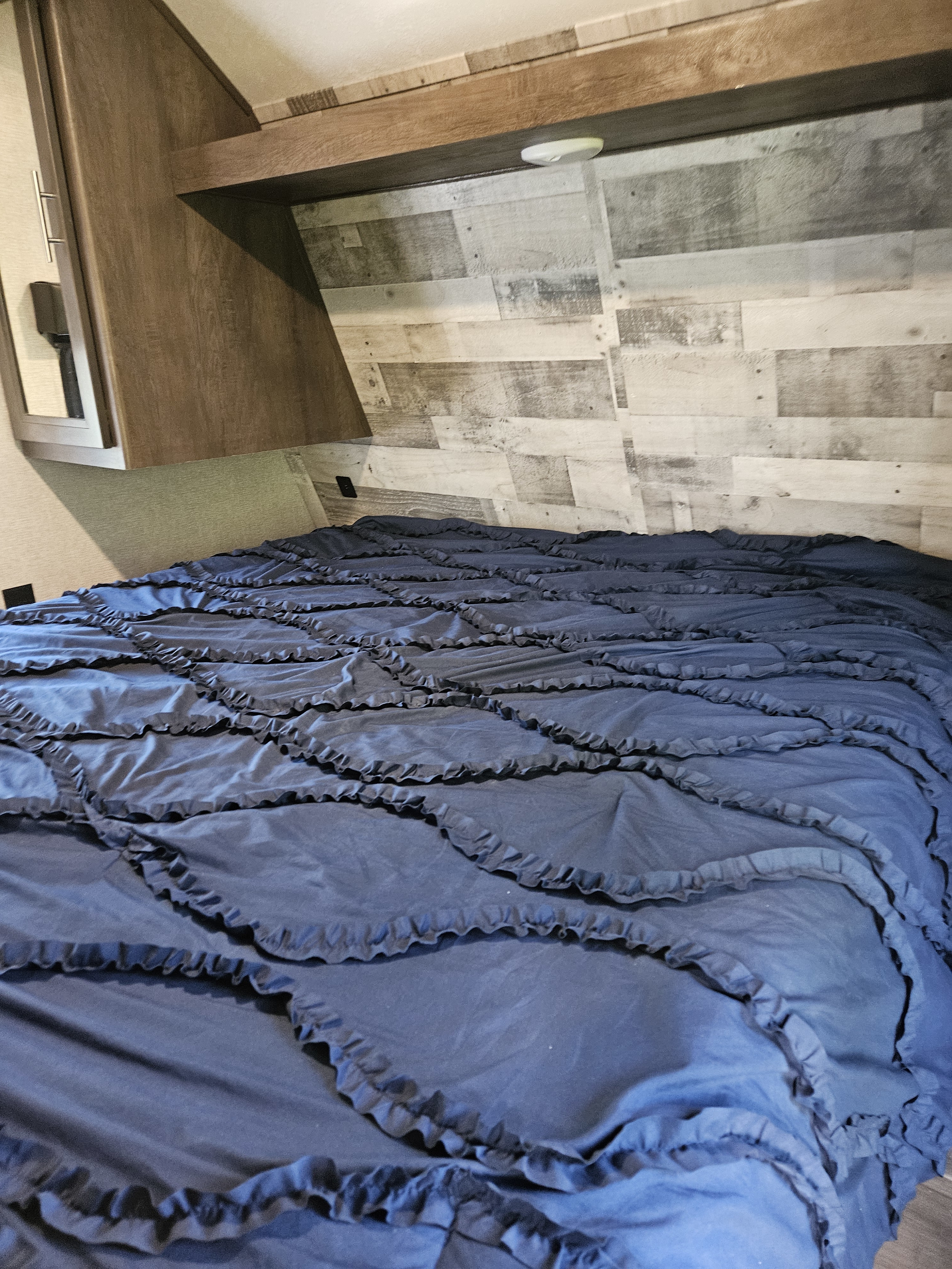 Cozy RV rental bedroom interior, featuring a dark blue ruffled comforter and wood-paneled headboard.. Coleman 263BHWE 2021