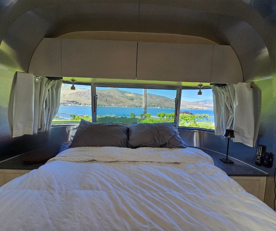 Airstream RV rental interior: cozy bedroom with panoramic lake and mountain views from large windows.. Airstream Flying Cloud 2023