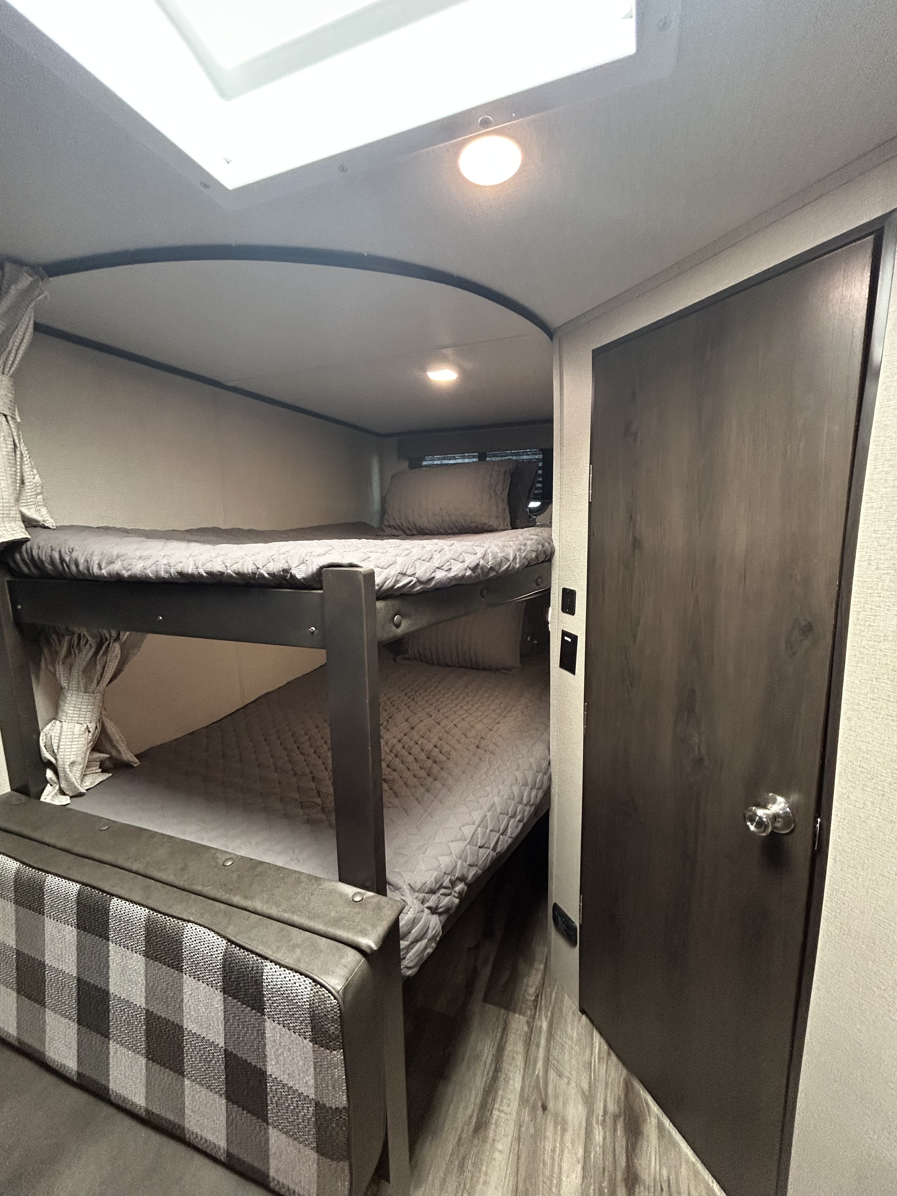 Cozy bunk beds in an RV rental, featuring quilted bedding, a ceiling light, and a nearby door. Ideal for families.. Grand Design Transcend Xplor 2022