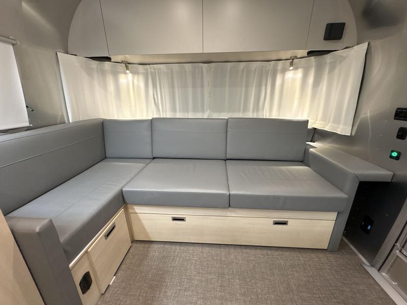 Cozy RV rental interior with L-shaped gray sofa, under-seat storage, and white curtains along the curved wall.. Airstream Flying Cloud 2023