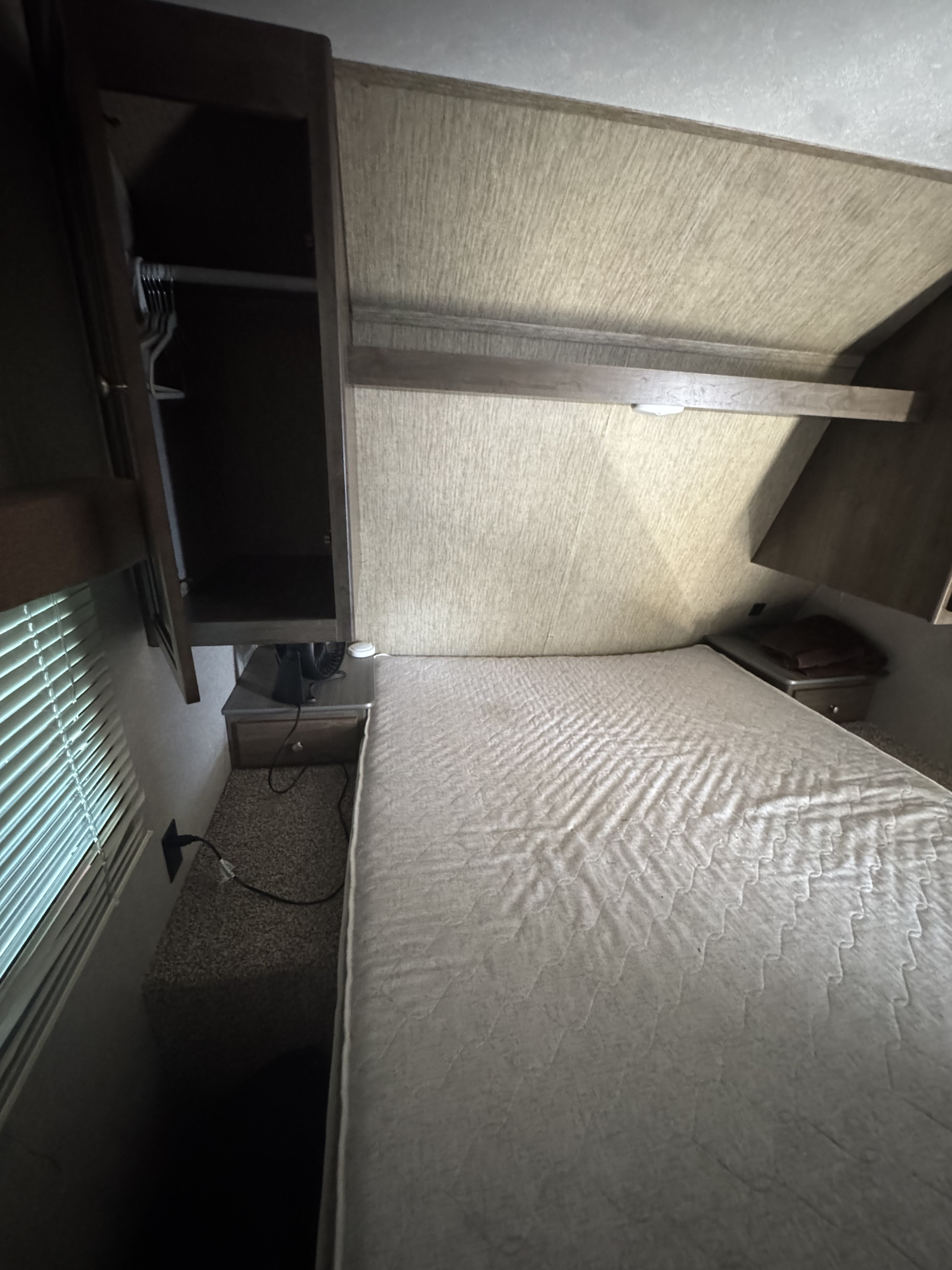 Interior view of an RV rental bedroom showing a bed, open closet, window with blinds, and nightstands.. Dutchmen Coleman Lantern 2018