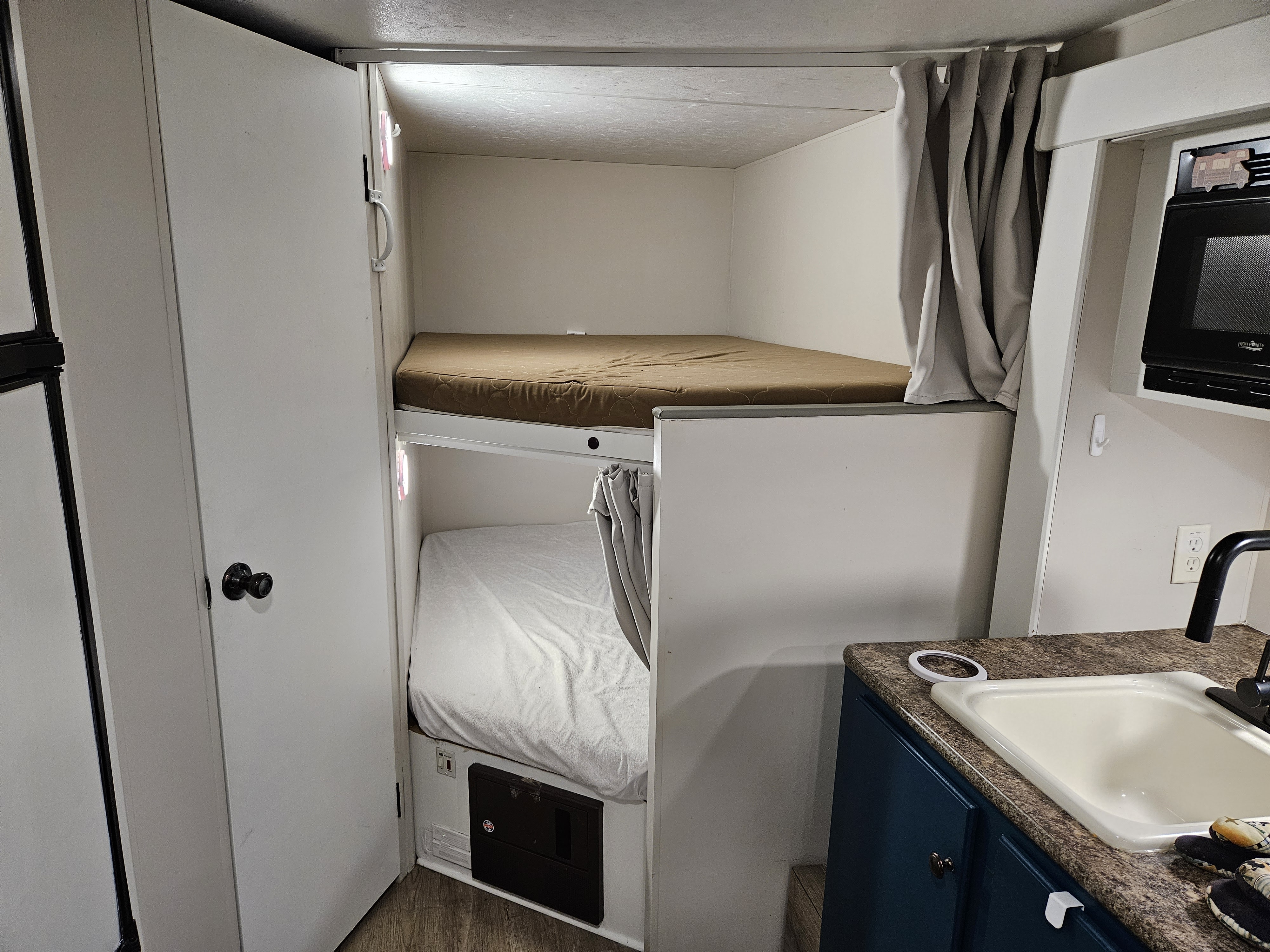 Interior of an RV rental: upper and lower bunk beds, plus a compact kitchen area with a sink and microwave.. Spree Escape 2014