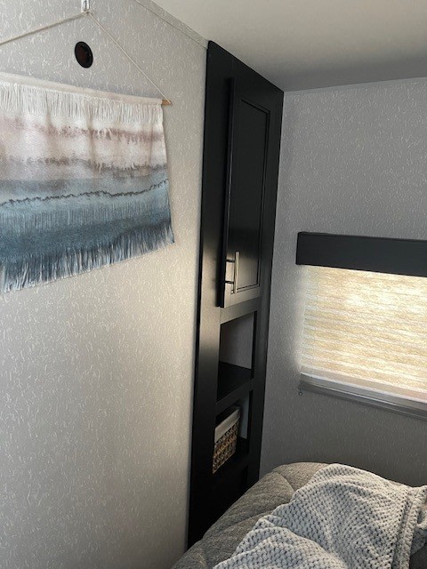 Cozy RV rental bedroom: showing a clever storage cabinet, wall hanging, and comfortable bed.. Forest River Cherokee 2022