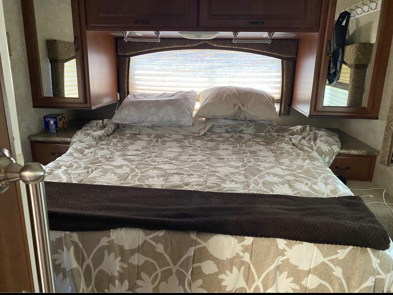 Spacious RV rental bedroom featuring a beige floral bed, pillows, overhead storage, and side tables.. Hurricane F53 2010