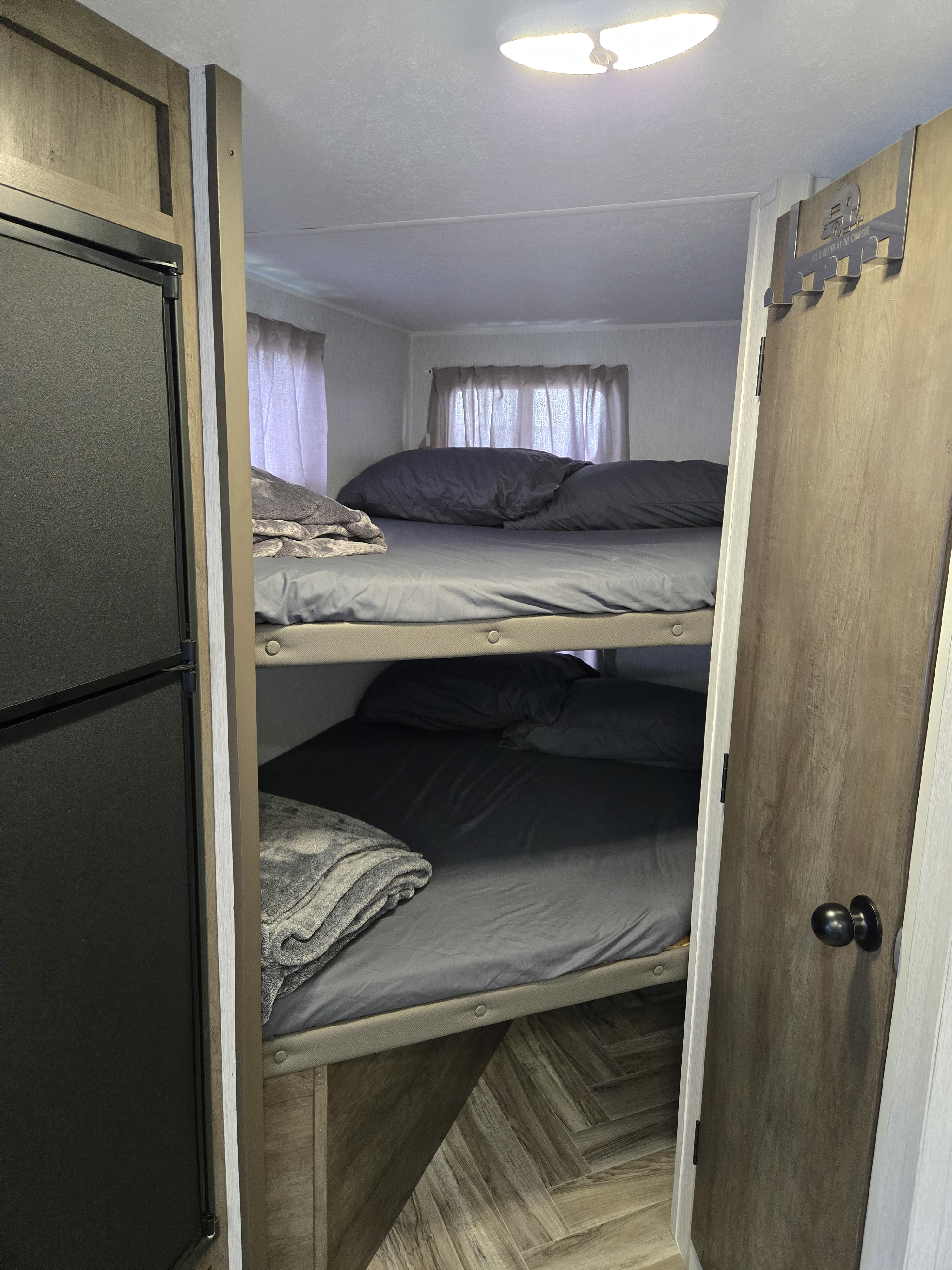 Cozy bunk beds in an RV rental, featuring dark gray bedding, a refrigerator on the left, and a decorative door hanger on the right.. Forest River EVO 178B 2022