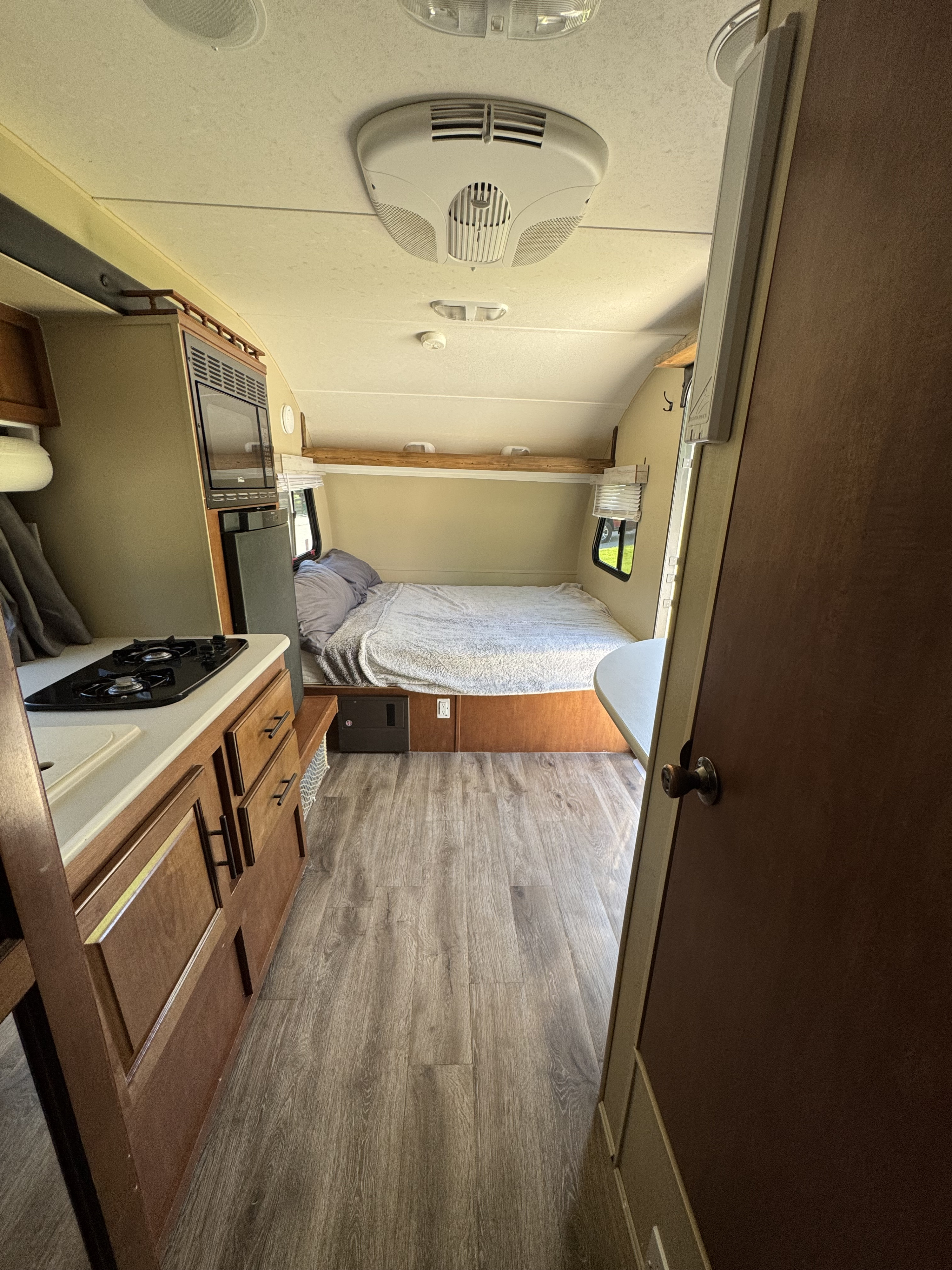 Interior view of an RV rental, featuring a compact kitchen on the left, a cozy bed at the rear, and wood-look flooring.. Forest River R-Pod 2013