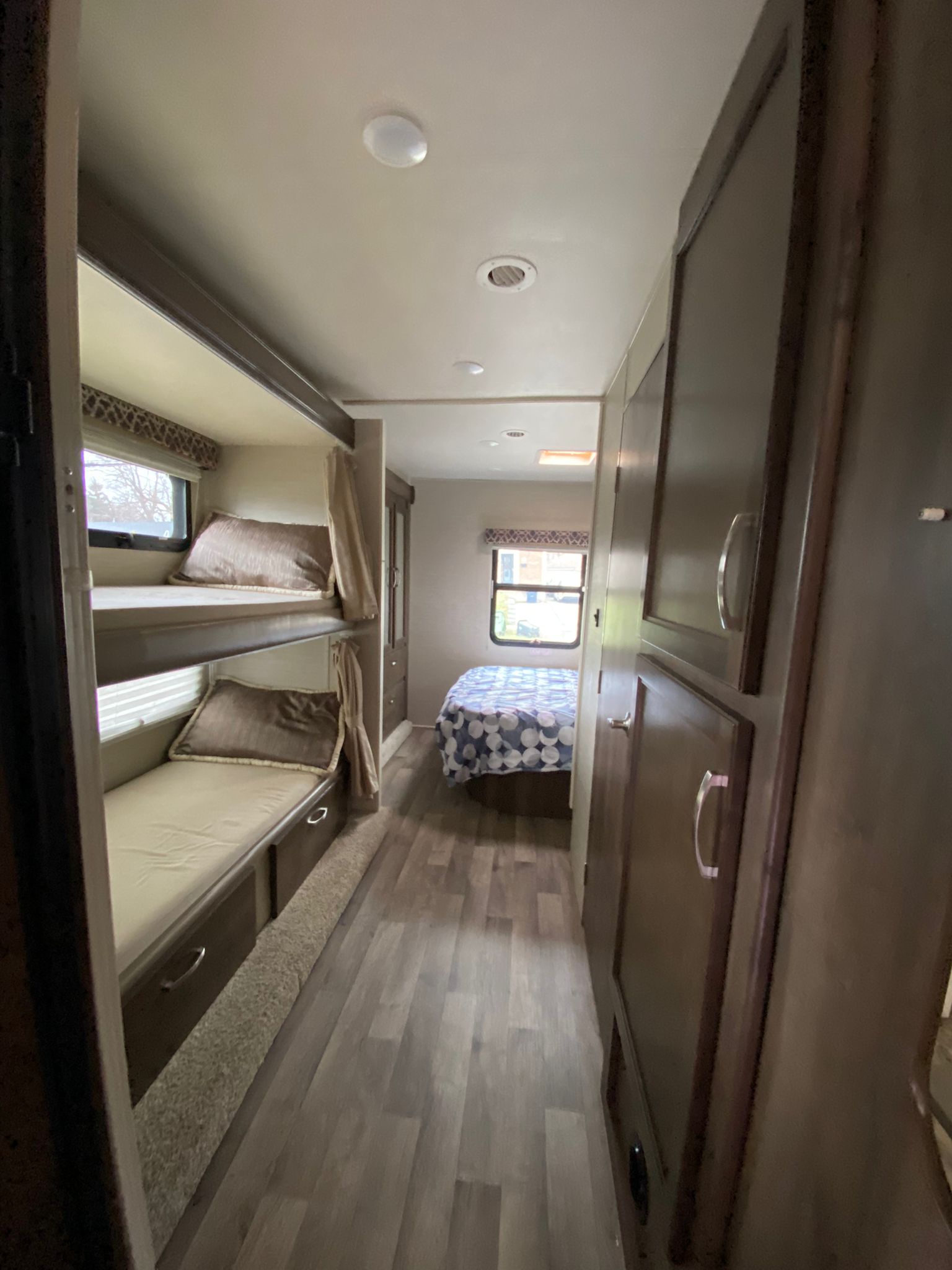 This RV rental interior shows bunk beds on the left, a hallway with dark cabinets, leading to a main sleeping area.. Jayco Redhawk 2018