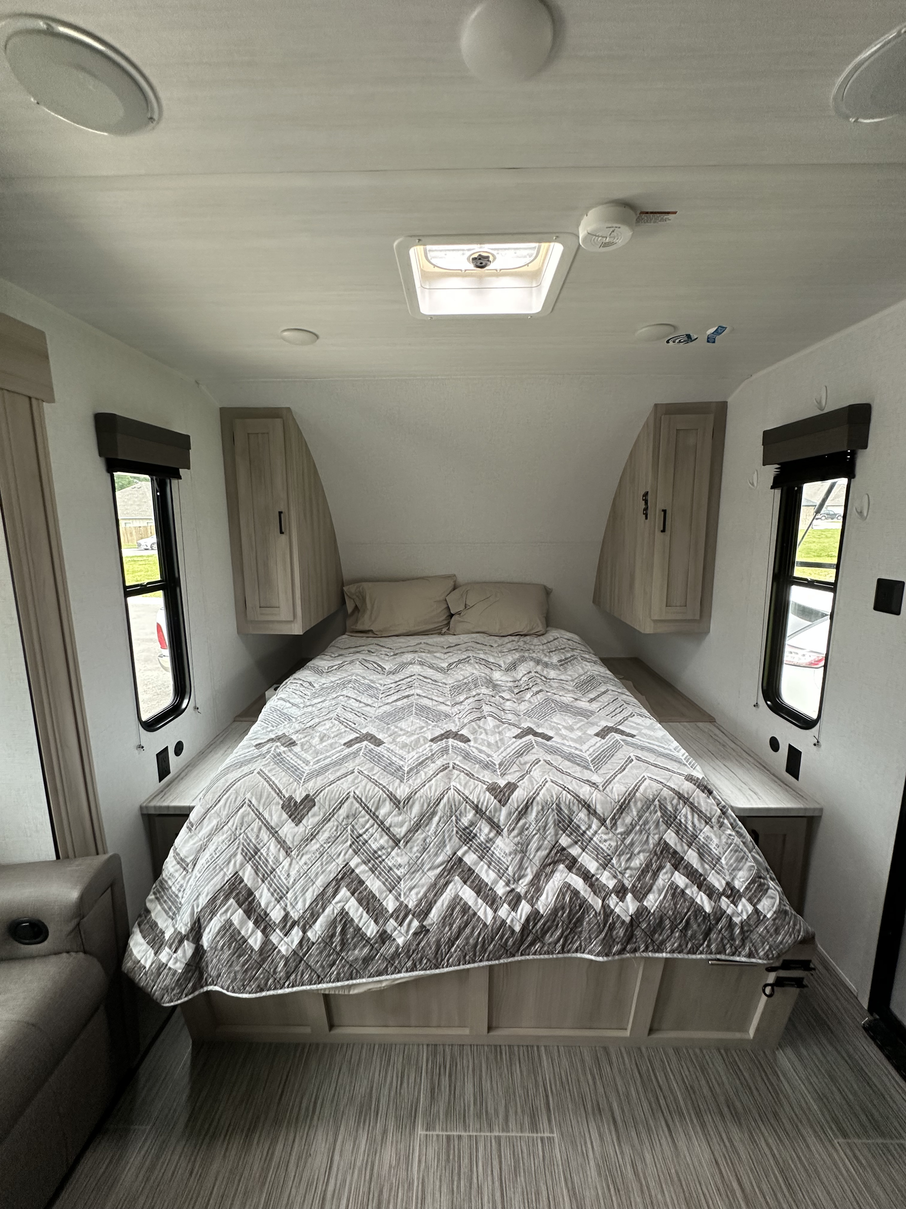 Cozy RV rental bedroom featuring a full bed, overhead cabinets, windows, and ceiling lights/vent for comfortable travel.. Forest River East to West 2024