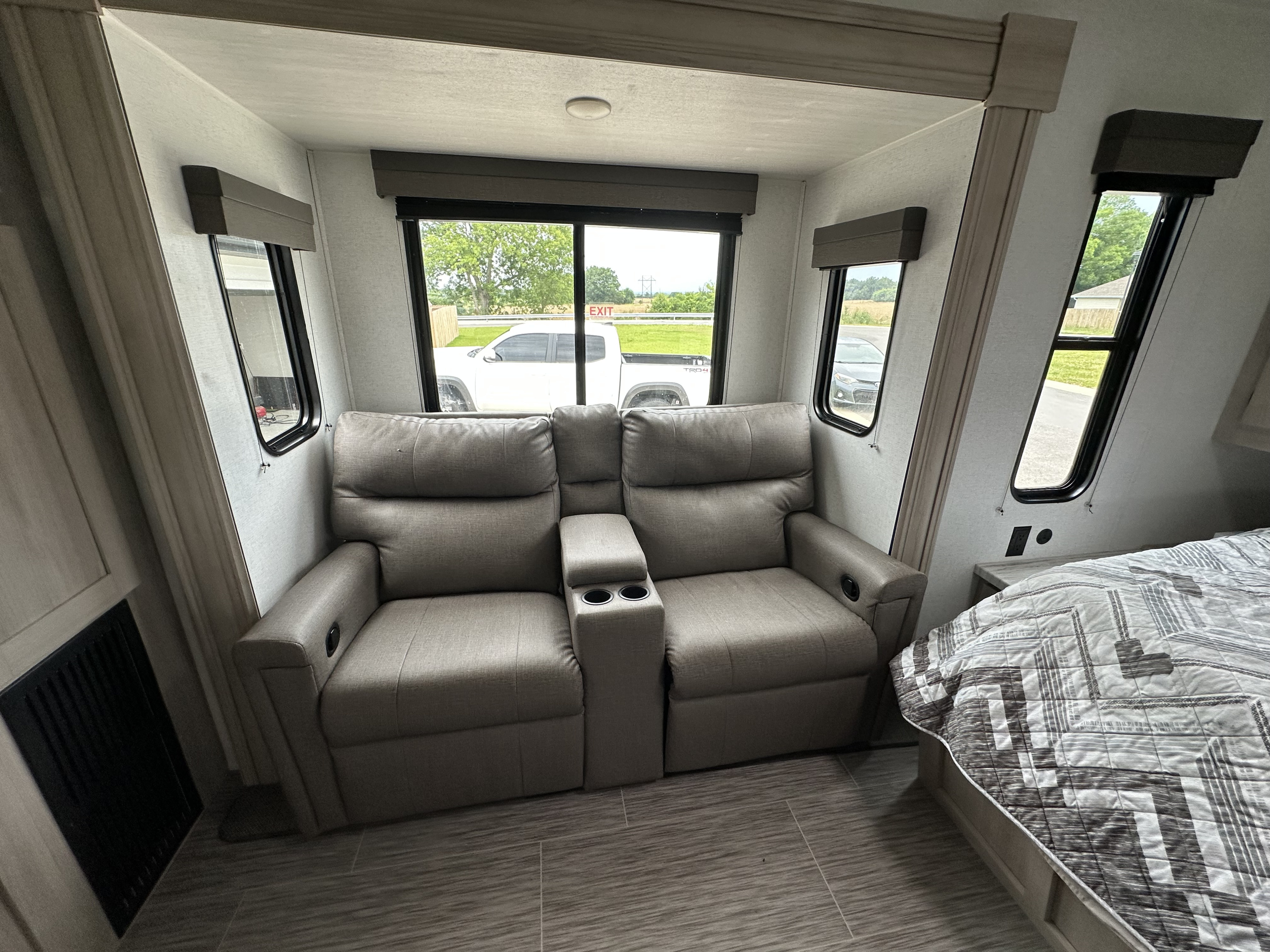 RV rental interior: Comfortable two-seater recliners with cup holders, a bed, and large windows revealing road views.. Forest River East to West 2024