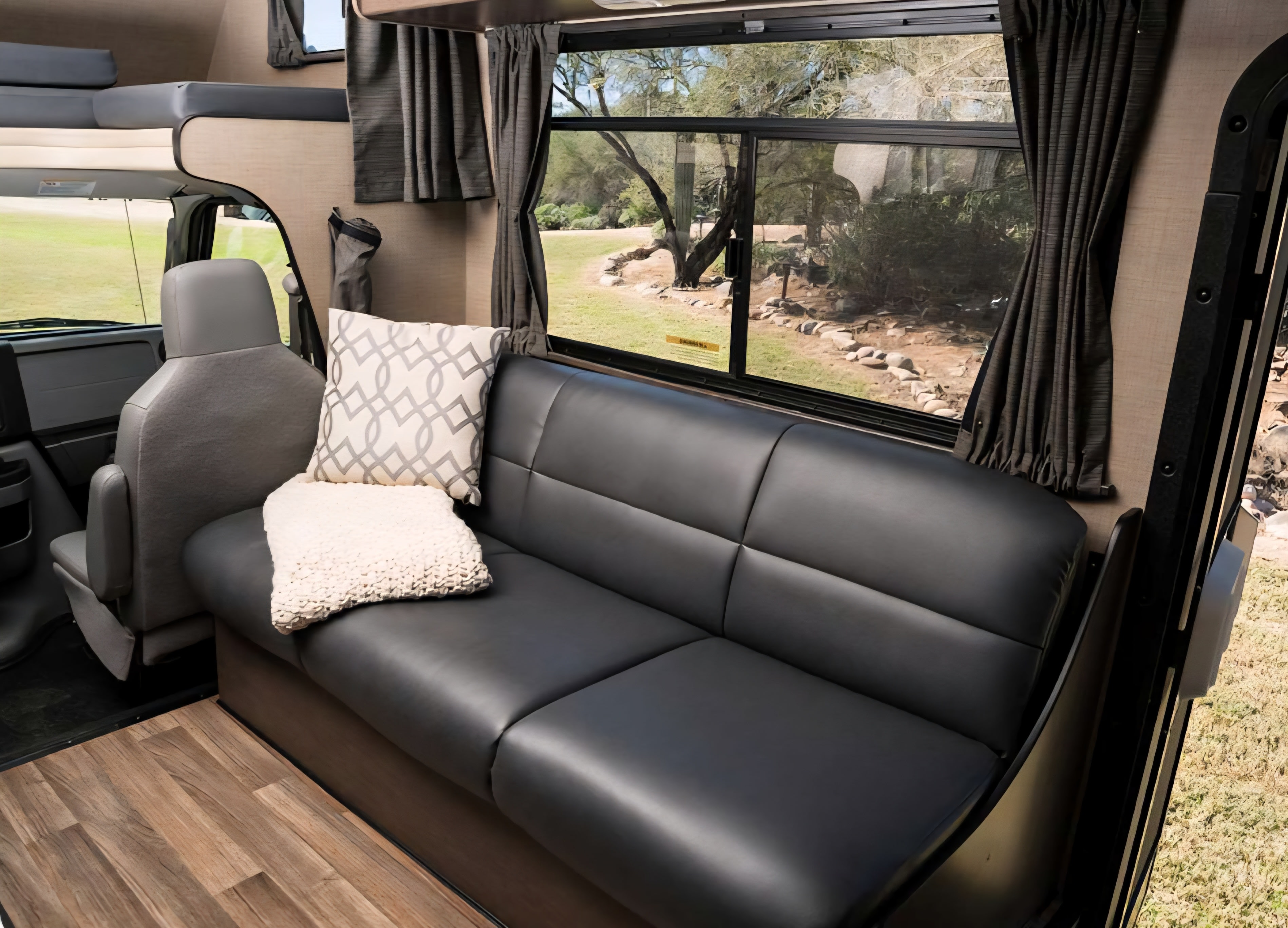 Spacious RV rental interior with a plush black sofa, decorative pillow, overhead bunk, and scenic window view.. Thor Majestic 2019