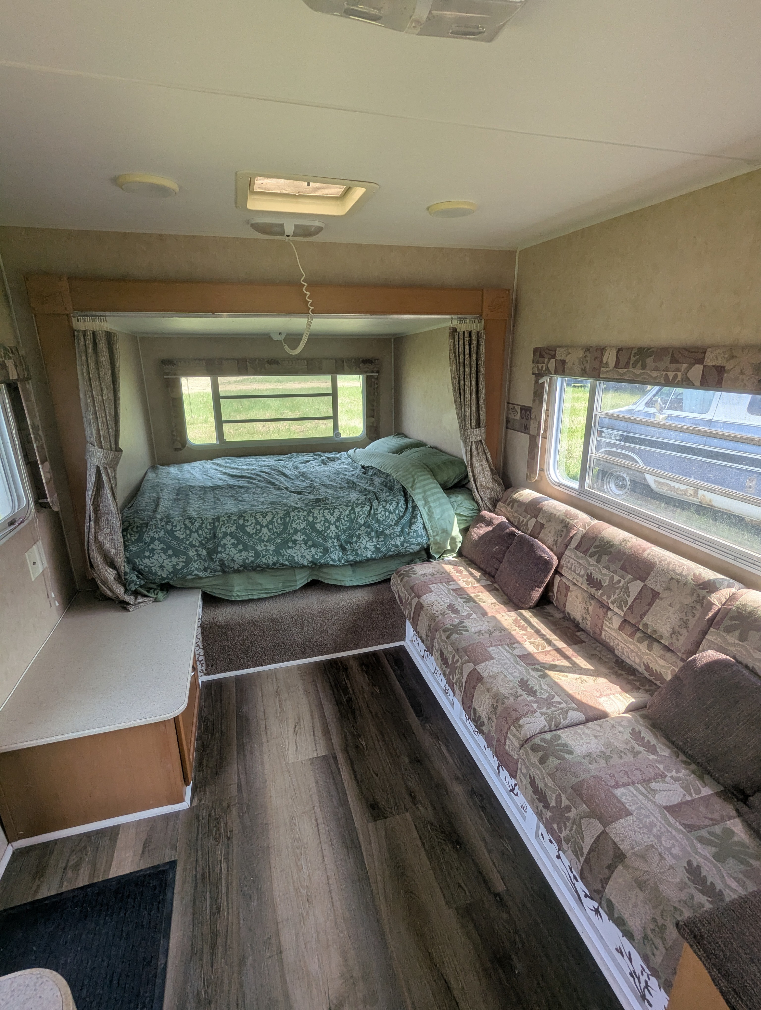 Cozy RV rental interior: features a comfortable bed with green bedding, a patterned sofa, and wood-look flooring.. Gulf Stream Ameri-Lite 2006