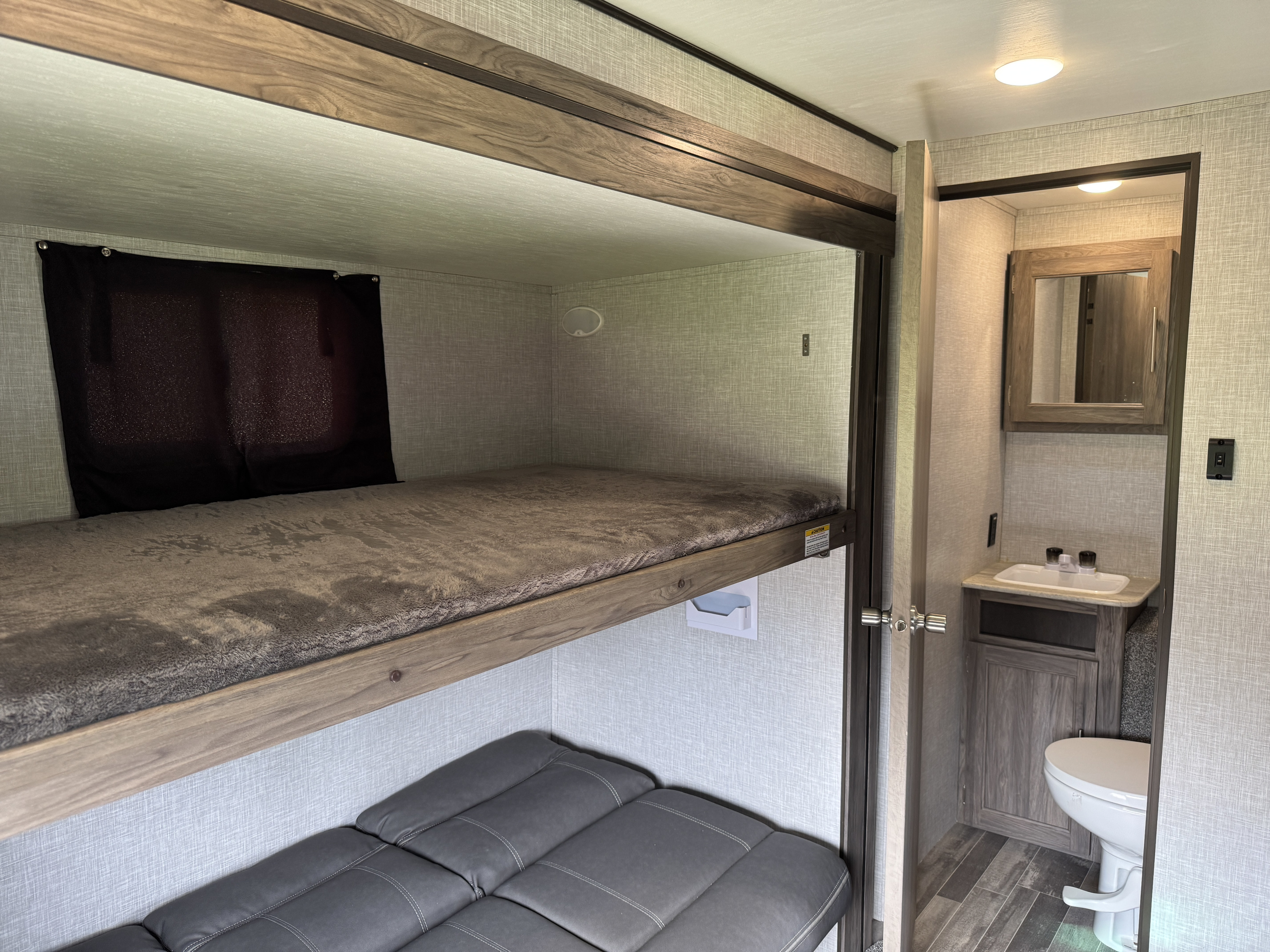 RV rental interior: bunk beds with gray bedding, a convertible sofa, and an accessible compact bathroom with sink & toilet.. Crossroads Zinger 2022