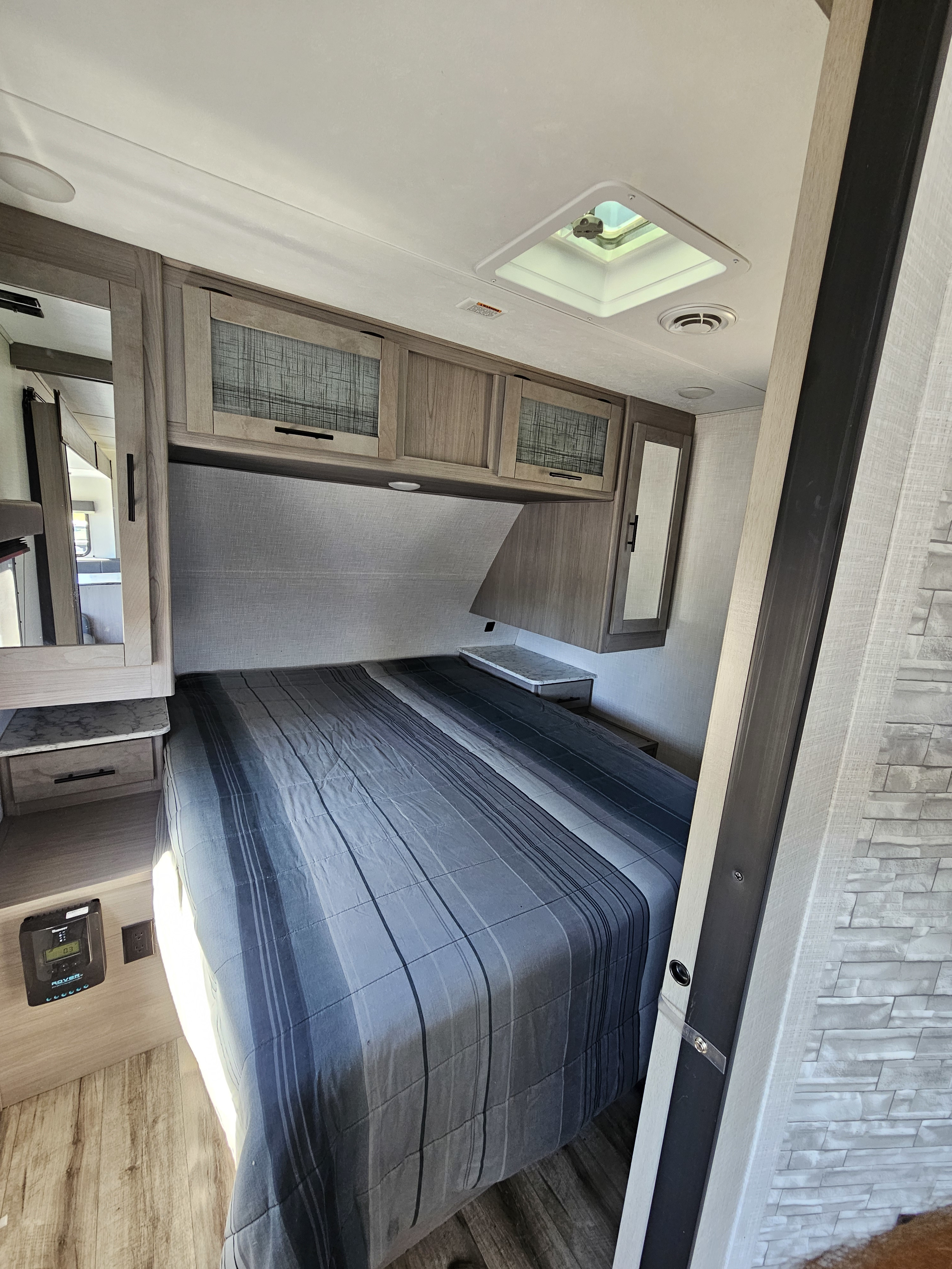 Inside an RV rental: a compact bedroom featuring a comfortable striped bed, overhead cabinets, and power outlets.. Dutchmen Coleman Light 2022