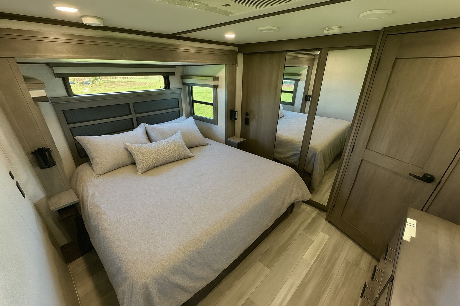 Spacious, modern RV rental bedroom with a comfy bed, mirrored closet doors, and scenic windows, perfect for travel.. Grand Design Solitude 2025