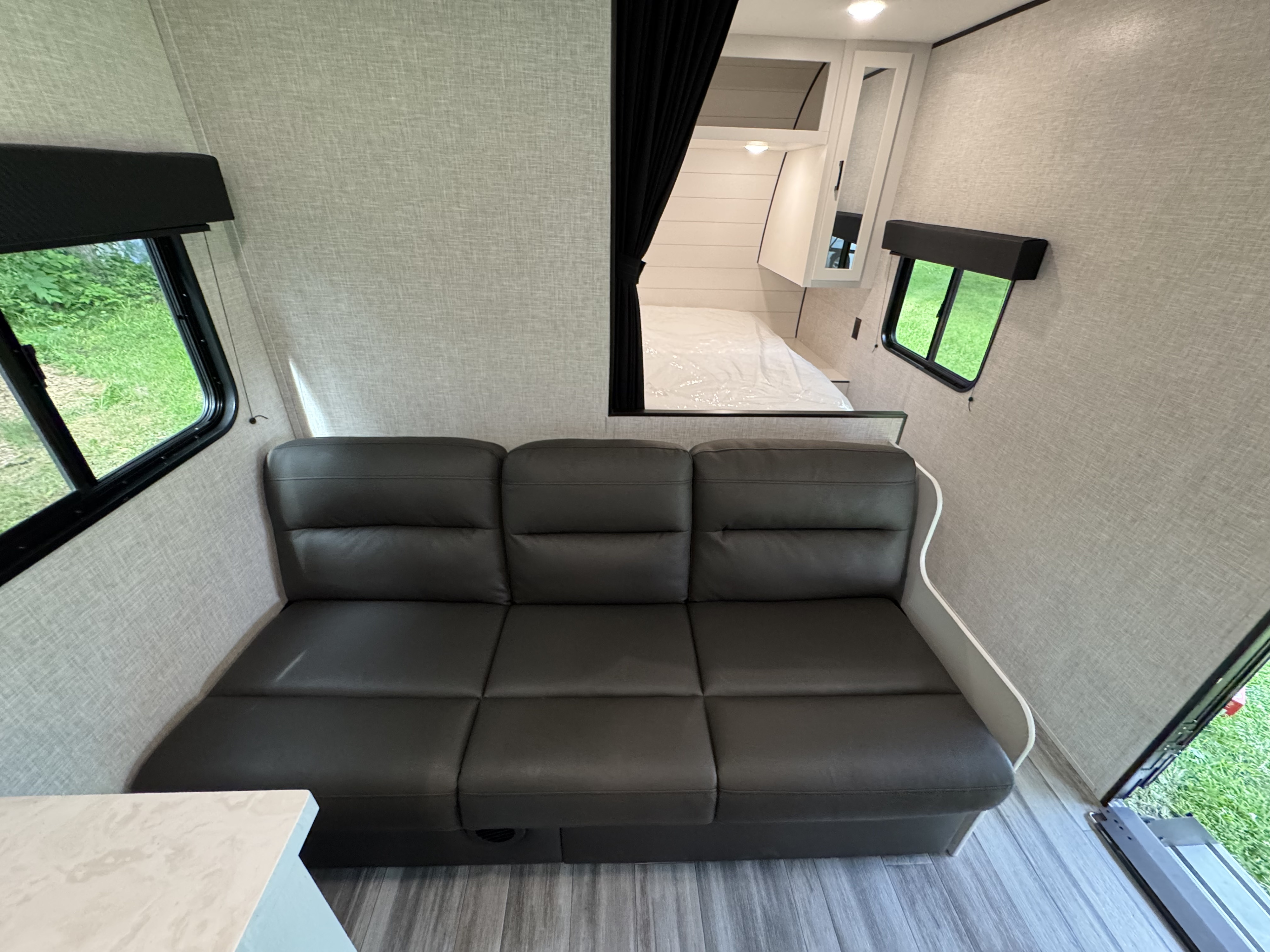 This RV rental interior shows a compact living space with a dark sofa, bright windows, and a separate bed area, ideal for travel.. Jayco Jay Flight SLX 2024
