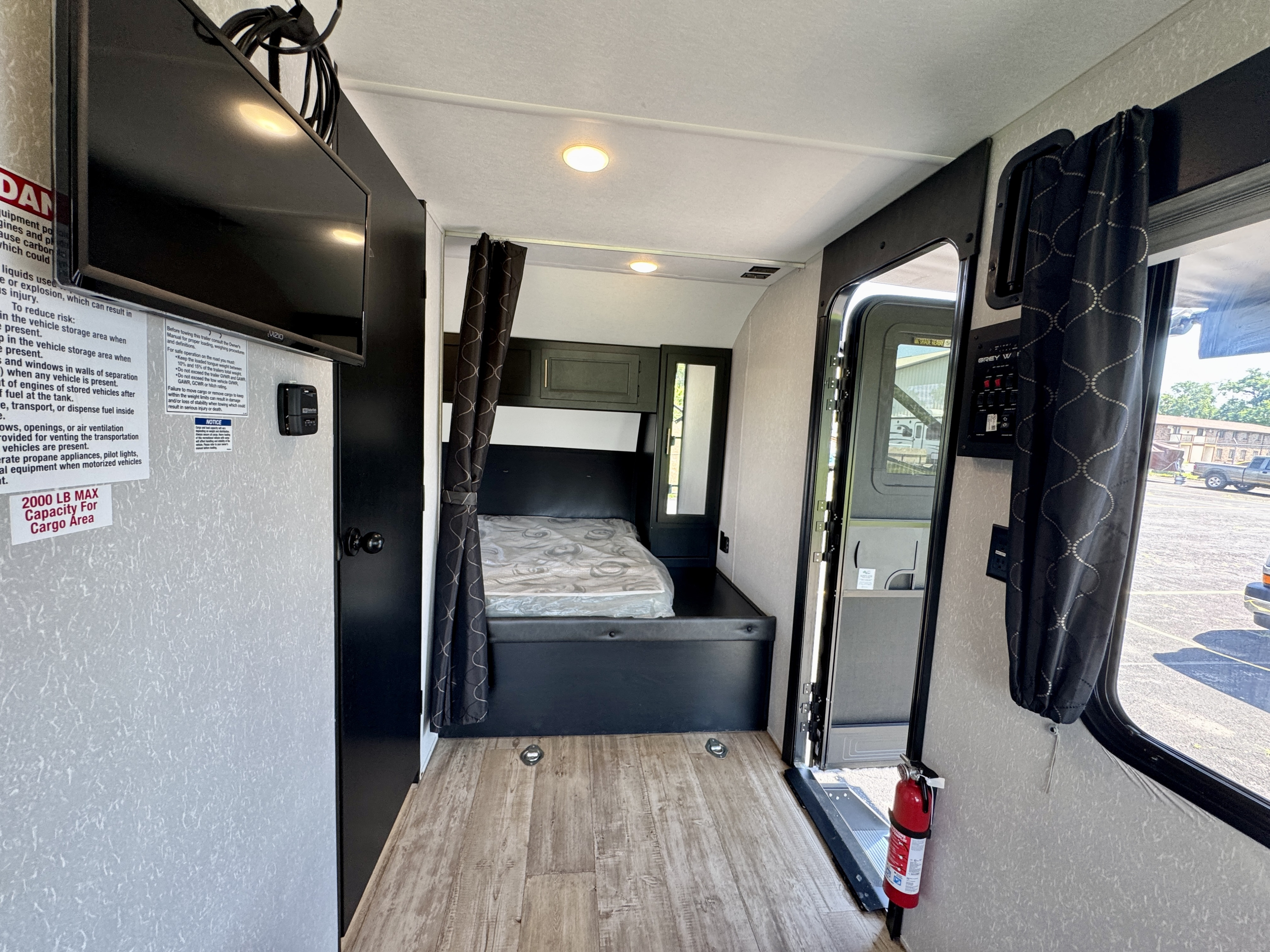 Spacious rv rental toy hauler interior, featuring a bed, Vizio TV, and wood-look floor with cargo tie-downs.. Forest River Grey Wolf 2021