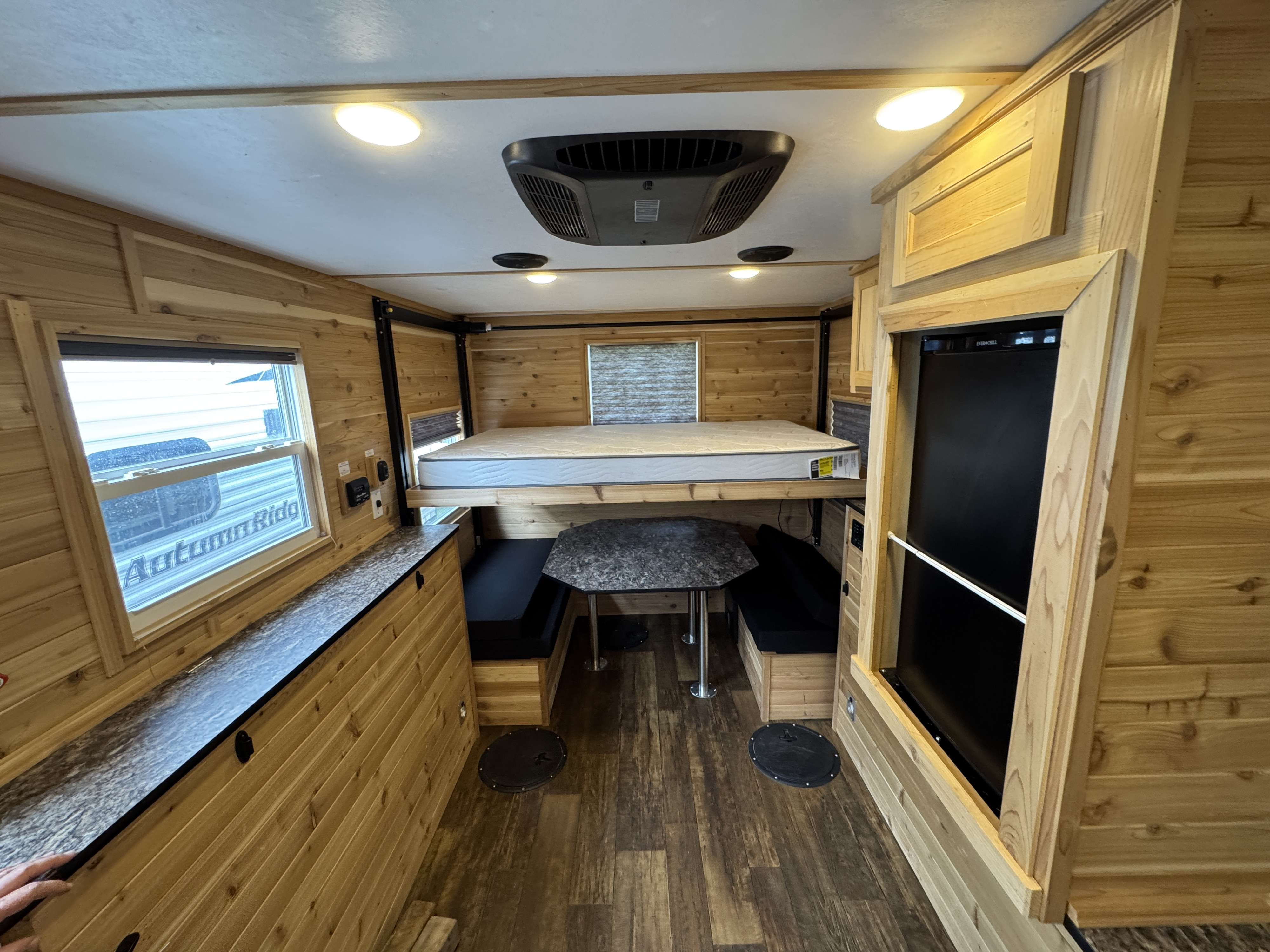 Detailed view of an **rv rental's** wooden interior: a convertible dinette, lift bed, fridge, and floor covers for versatile use.. Ice Castle Fish Houses Ice Castle Fish Houses Trailer 2023