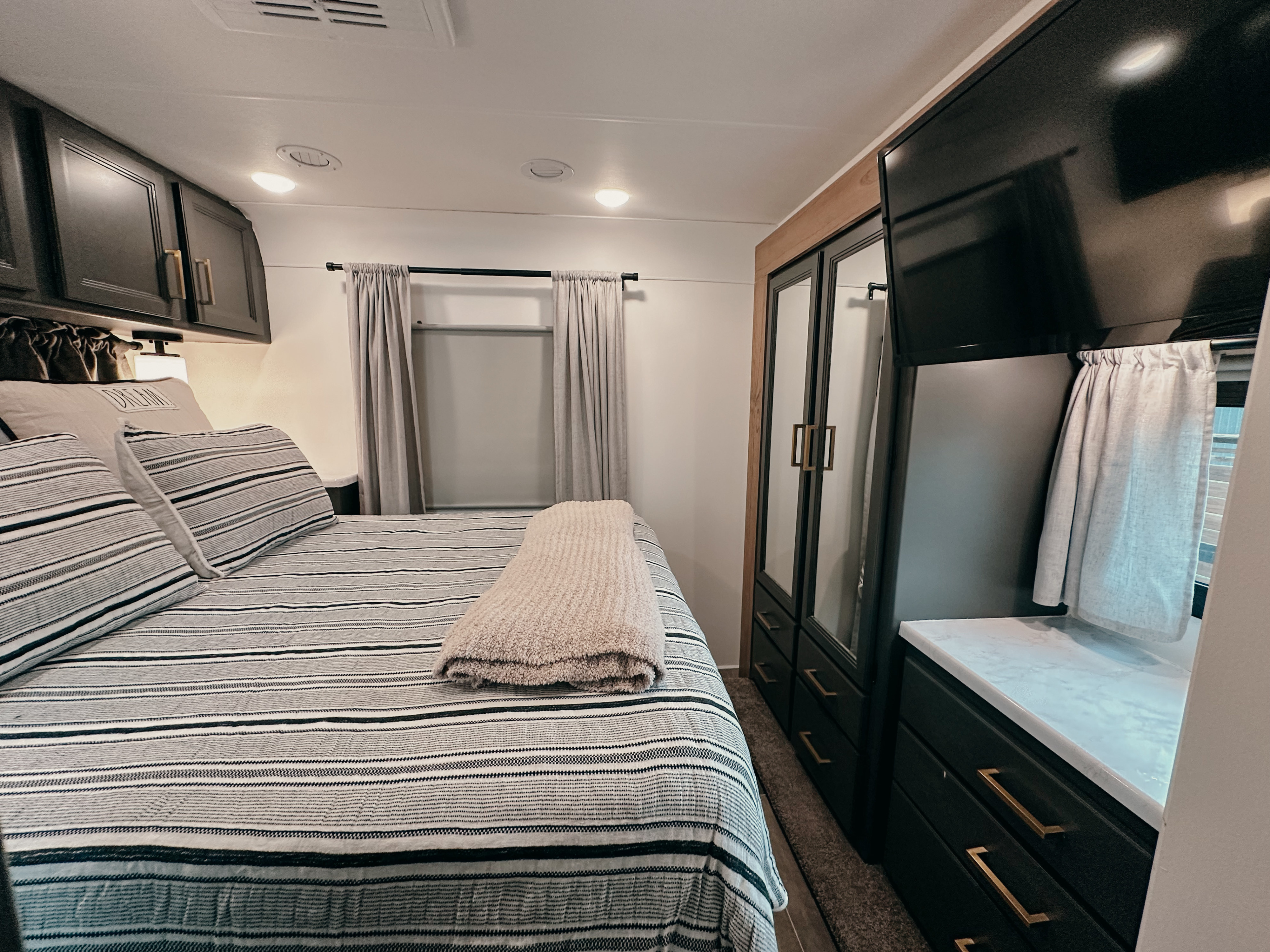 Cozy RV rental bedroom featuring striped bedding, overhead cabinets, and entertainment for your travels.. Thor Chateau 2022