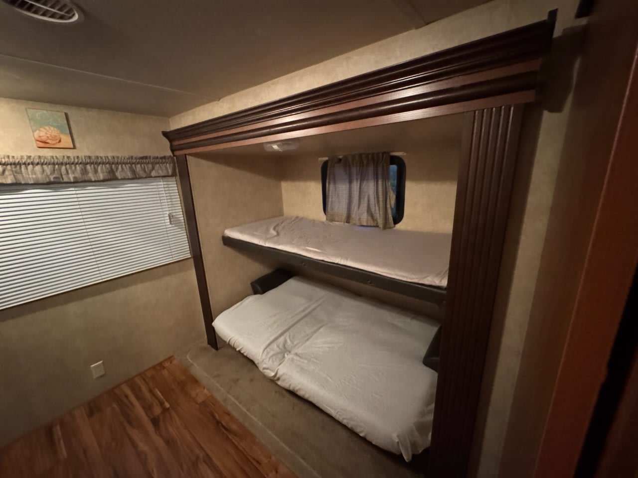 Inside an RV rental, featuring stacked bunk beds with light bedding, a large window with blinds, and wood floors. Ideal for family trips.. Forest River Salem 2016