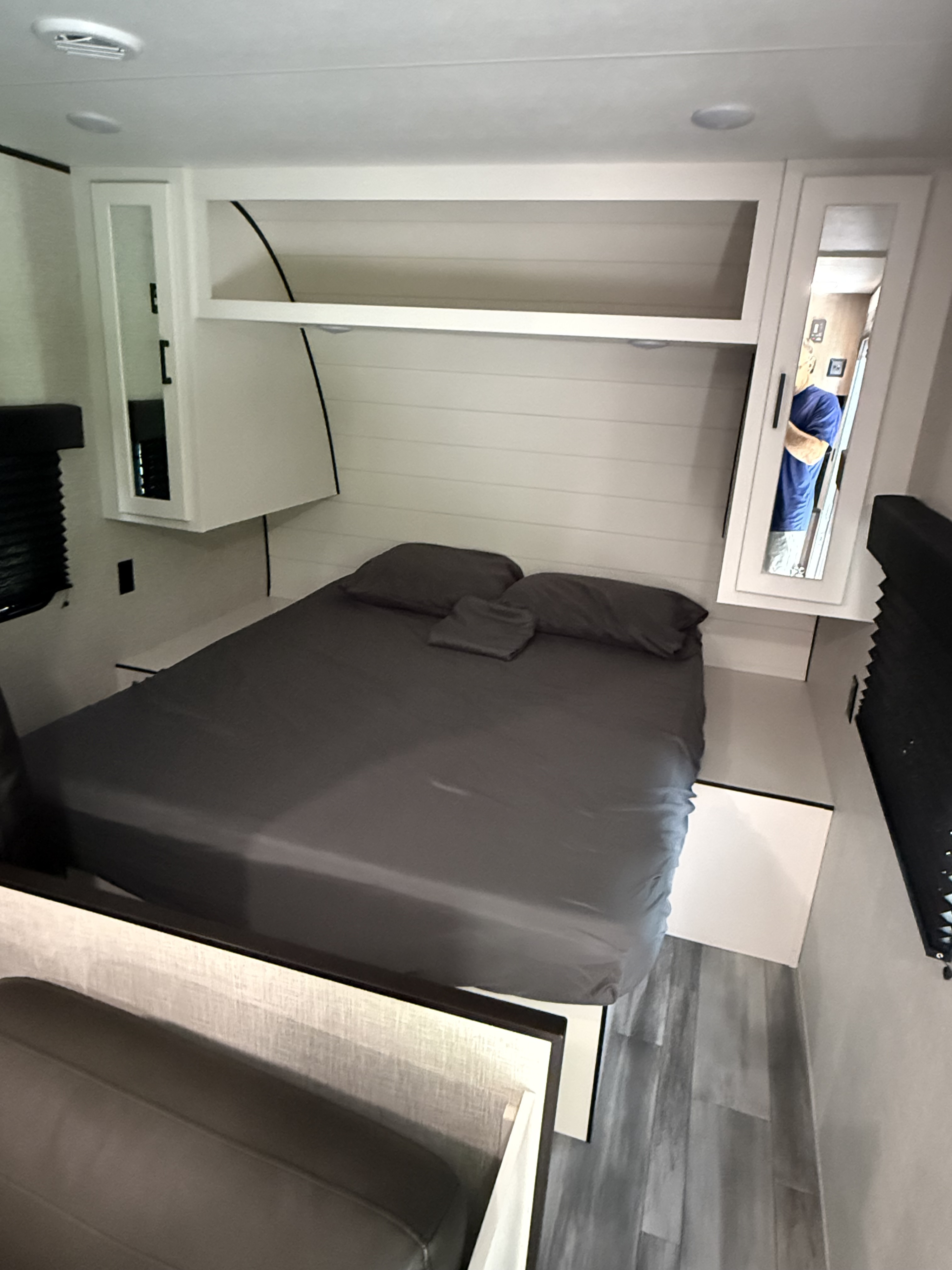 Inside an RV rental: a modern bedroom with a comfortable grey bed, built-in overhead storage, and practical mirrored cabinets.. Jayco Jay Flight SLX 2024