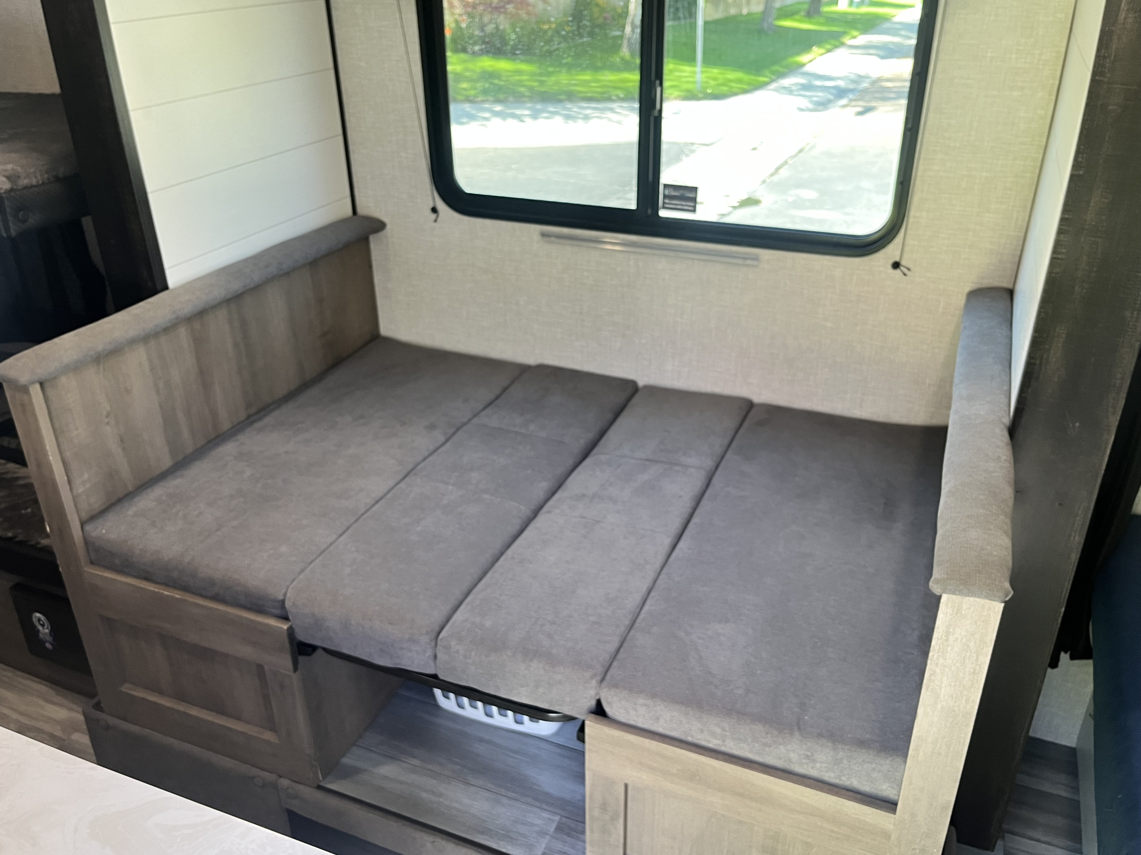 RV rental's dinette converts to a grey bed. Cozy interior with wood trim and a window view.. Jayco Jay Flight SLX Baja Edition 2024