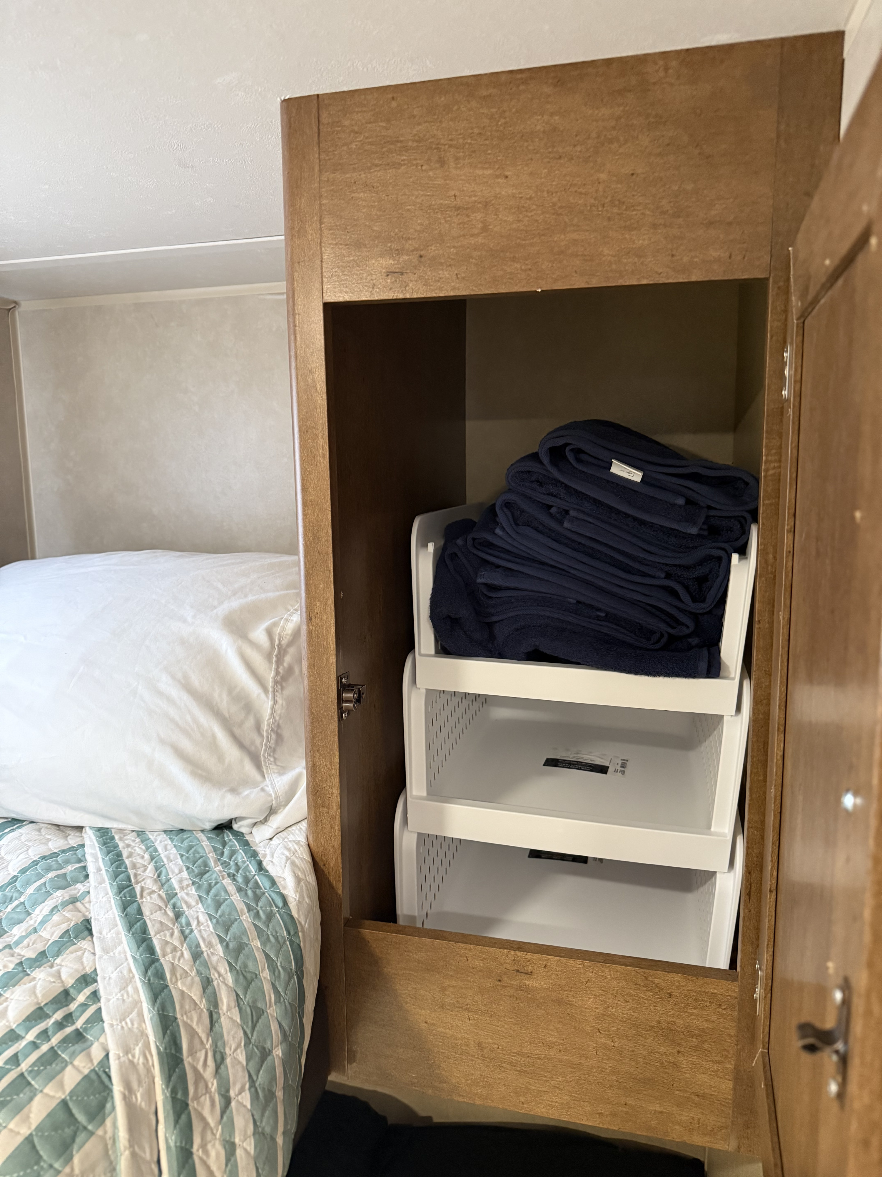 RV rental storage: Open cabinet with white stacking bins holding navy towels, beside a bed.. Forest River Salem Cruise Lite 2017