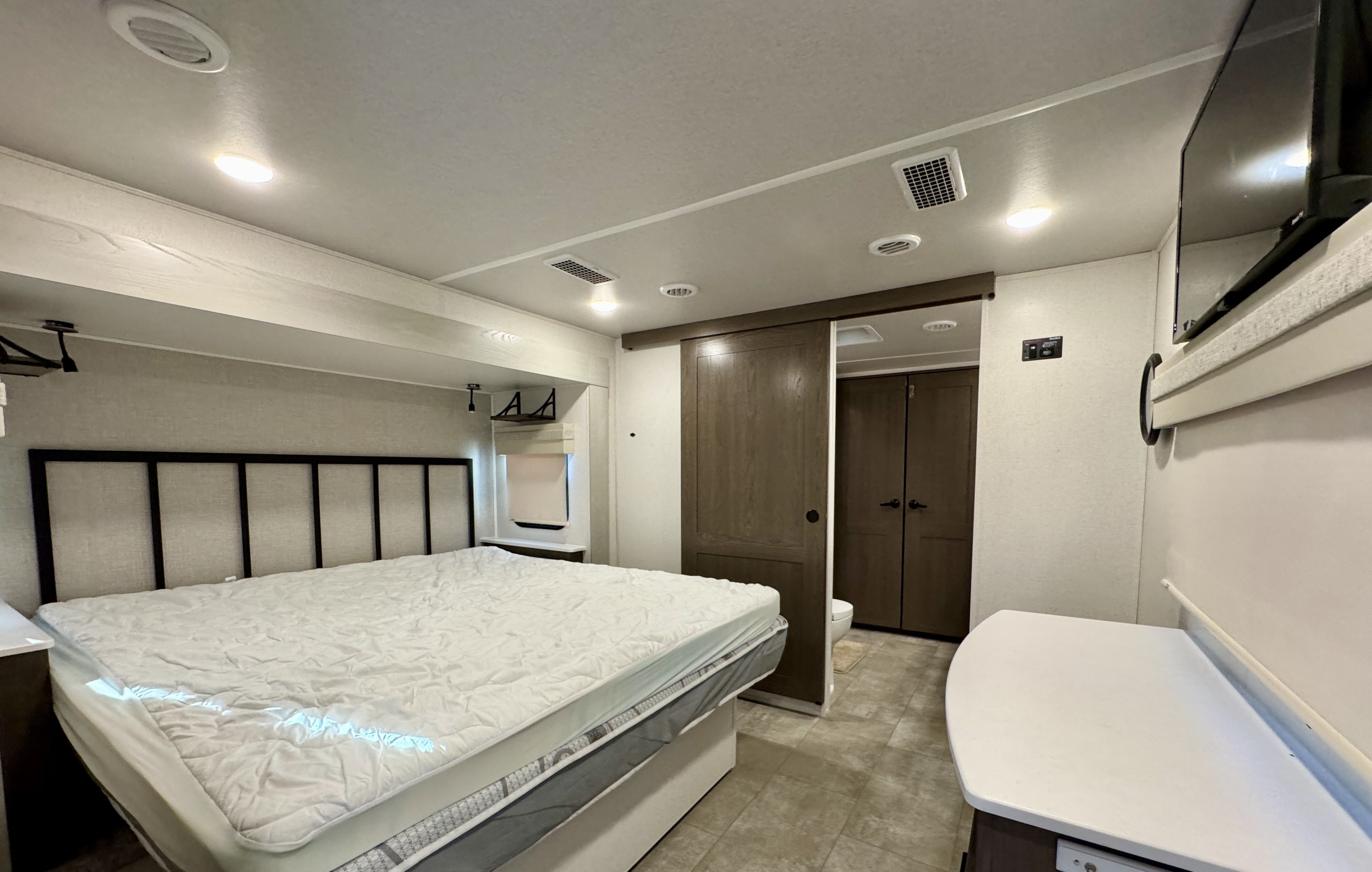 Spacious RV rental bedroom featuring a queen bed, modern lighting, and a sliding door for bathroom access, offering travel comfort.. Forest River Palomino Columbus 2023