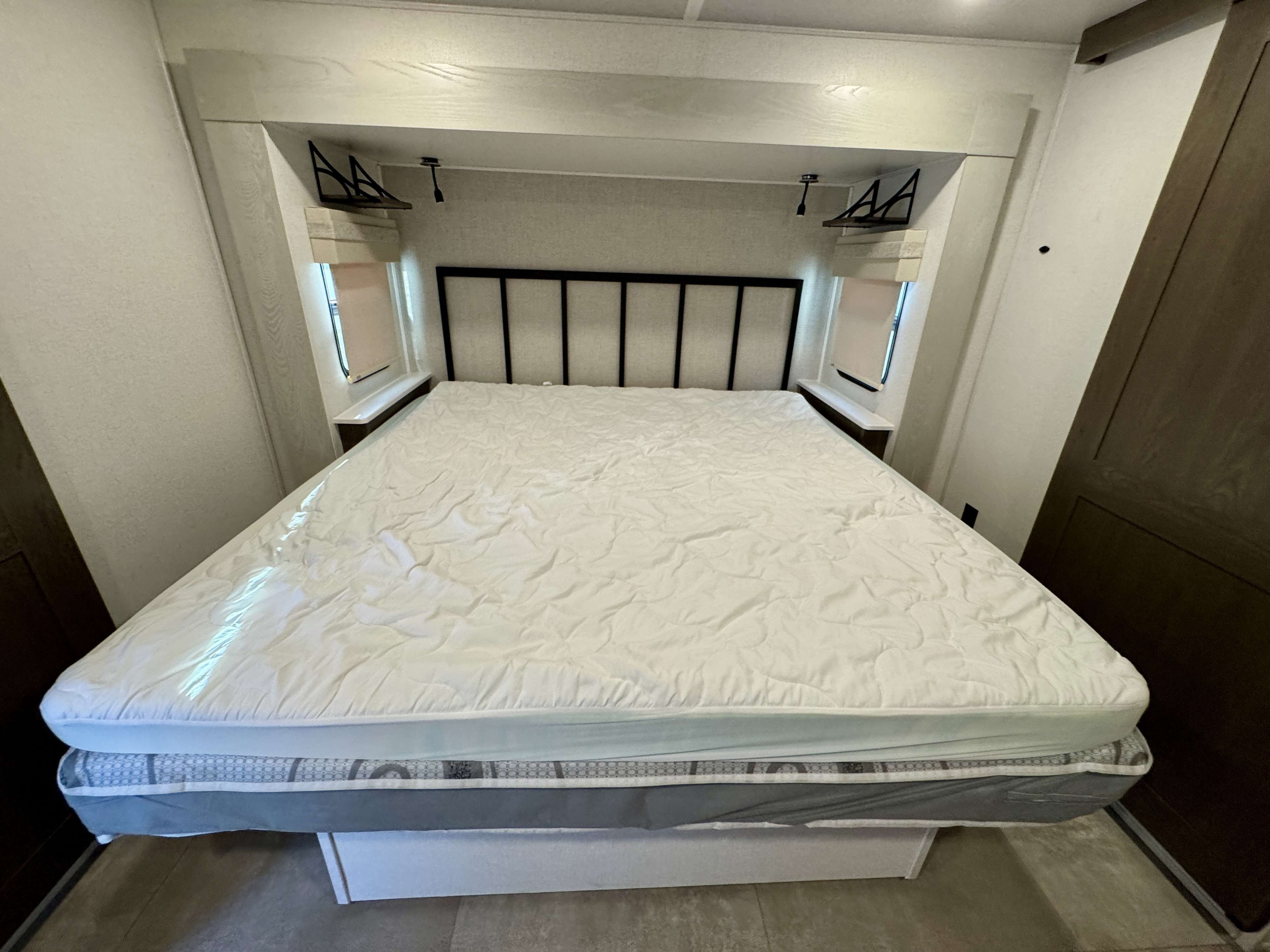 Clean RV rental bedroom featuring a queen bed with a white mattress pad, built-in shelving, and windows.. Forest River Palomino Columbus 2023