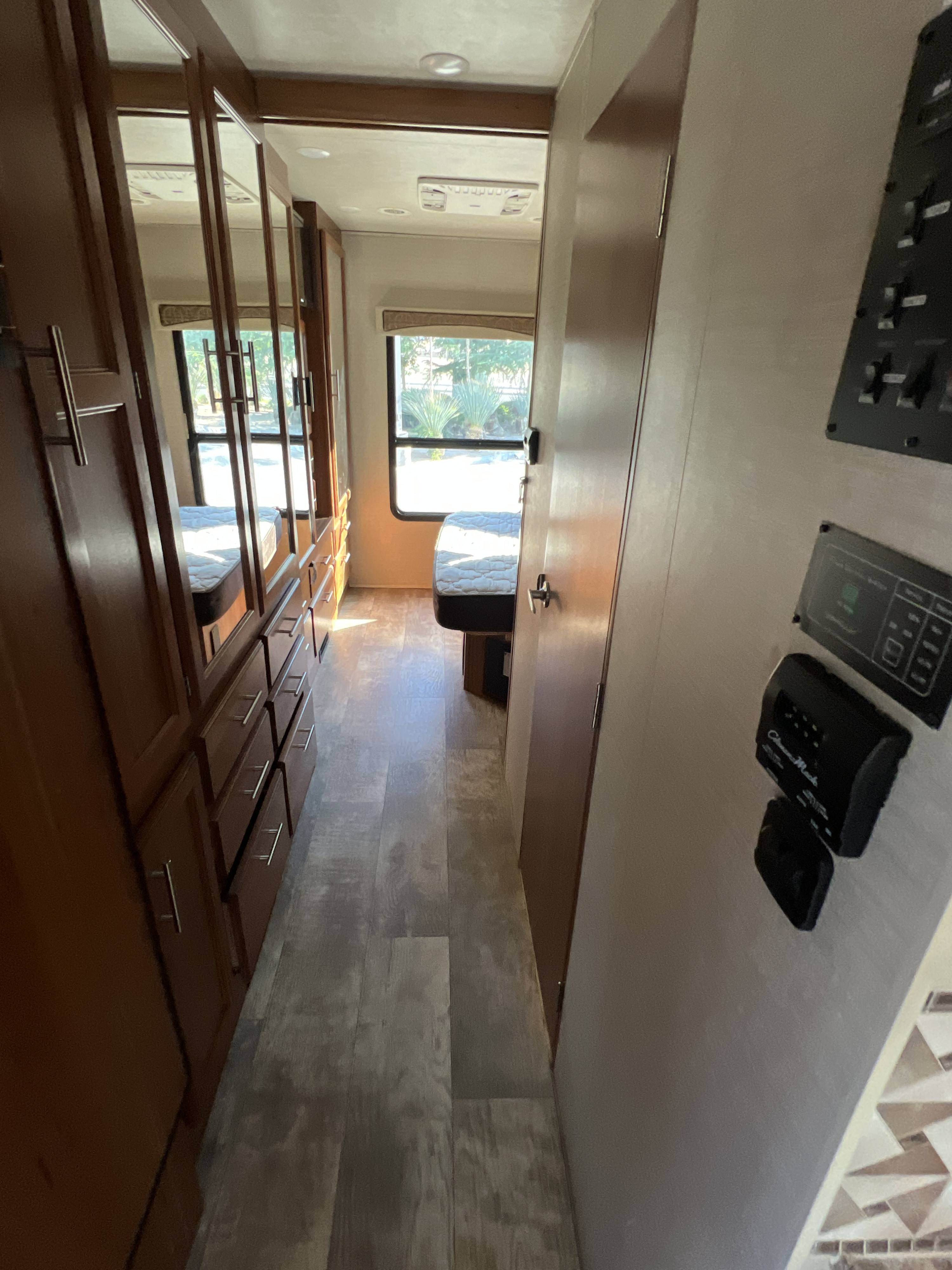 An RV rental bedroom shows a bed under a window with outdoor view, wood flooring, mirrored cabinets, and control panels.. Jayco Alante 2017