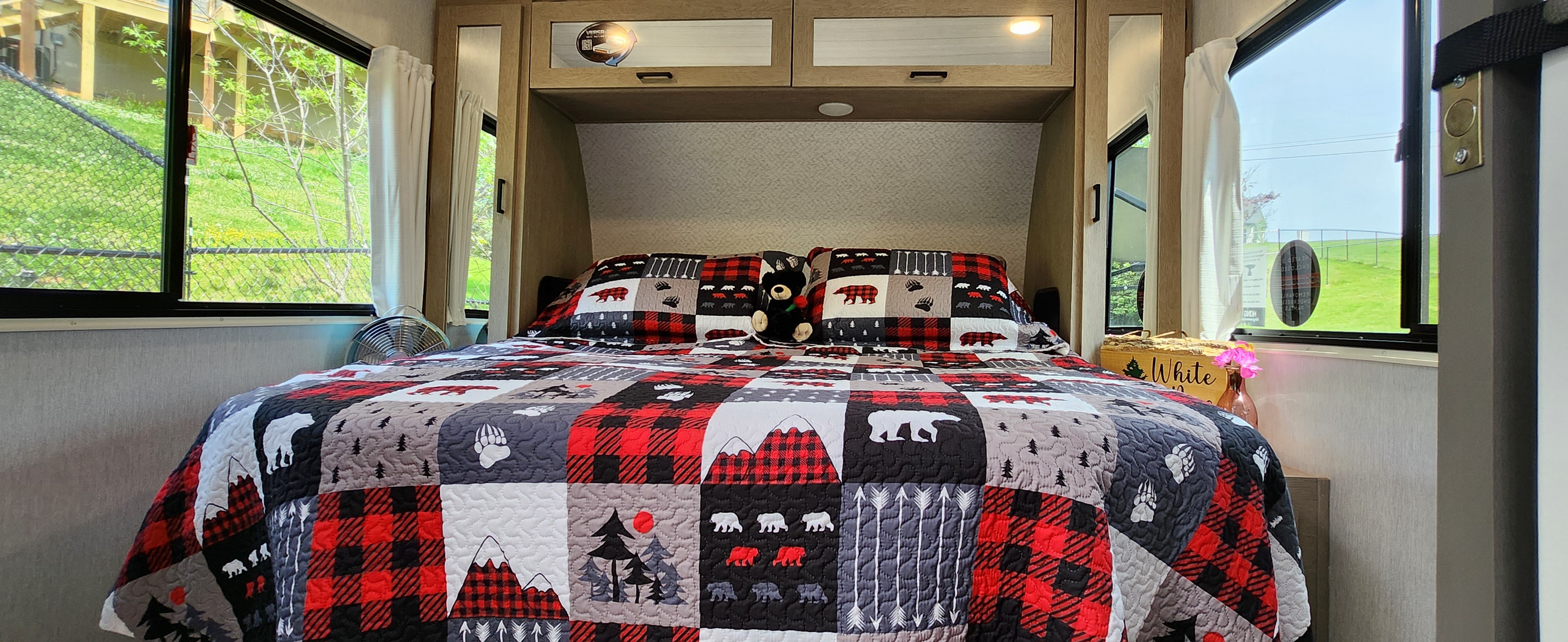 Cozy RV rental bedroom featuring a bear-themed quilt, overhead cabinets, and bright window views.. Forest River Wildwood Platinum 2024