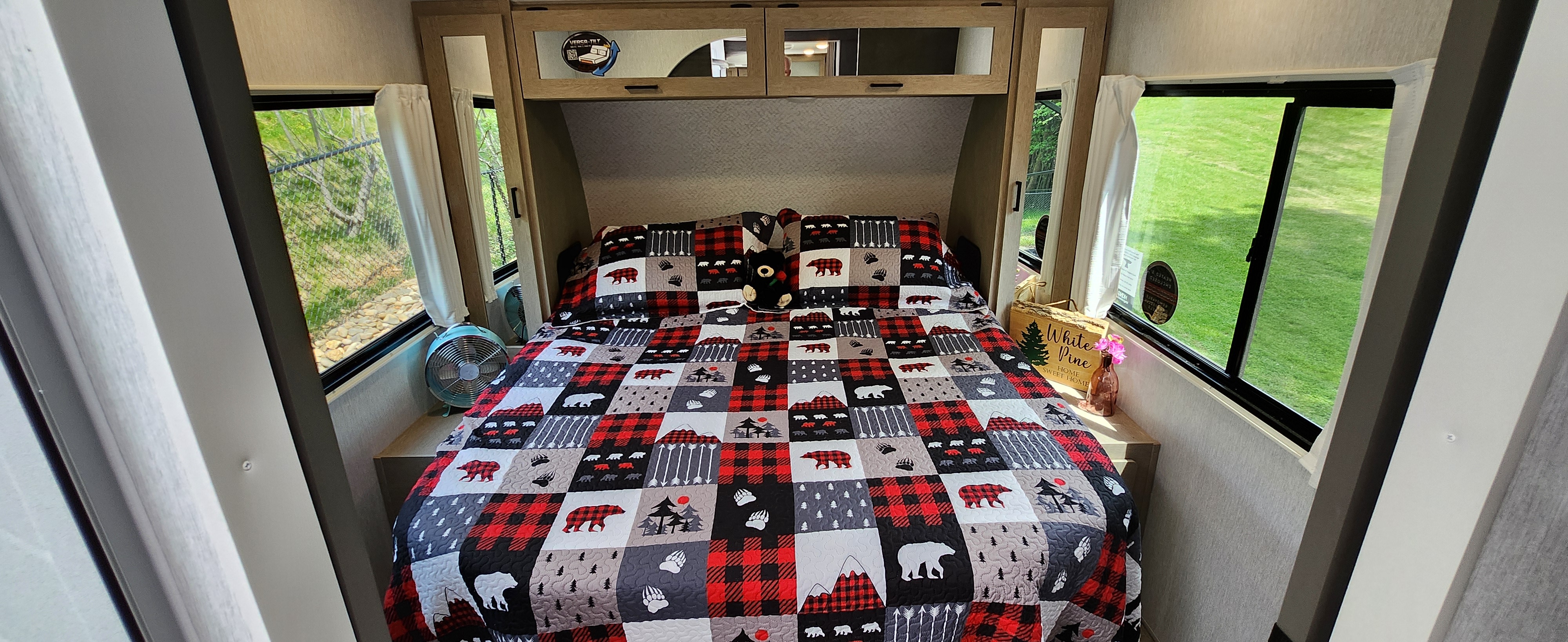 Cozy RV rental bedroom featuring a charming bear-themed quilt, side tables, and bright windows with natural views.. Forest River Wildwood Platinum 2024